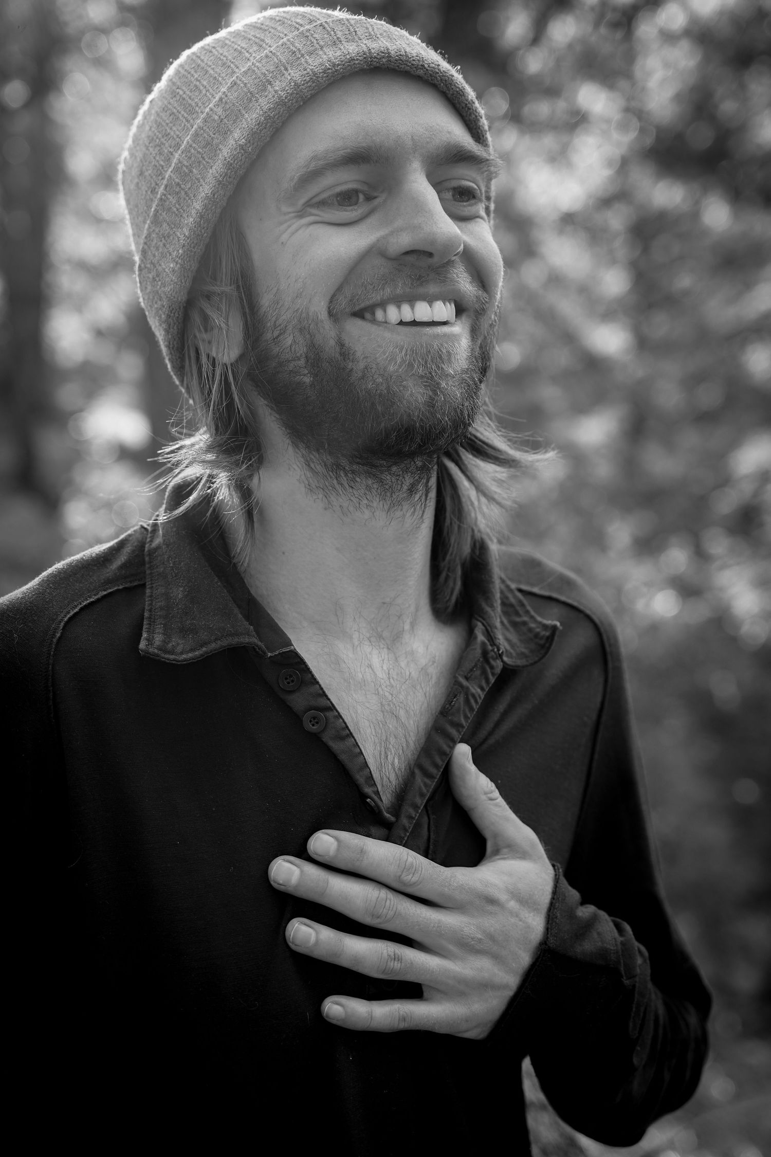 A candid black and white portrait of someone in a beanie and button-down shirt outdoors.