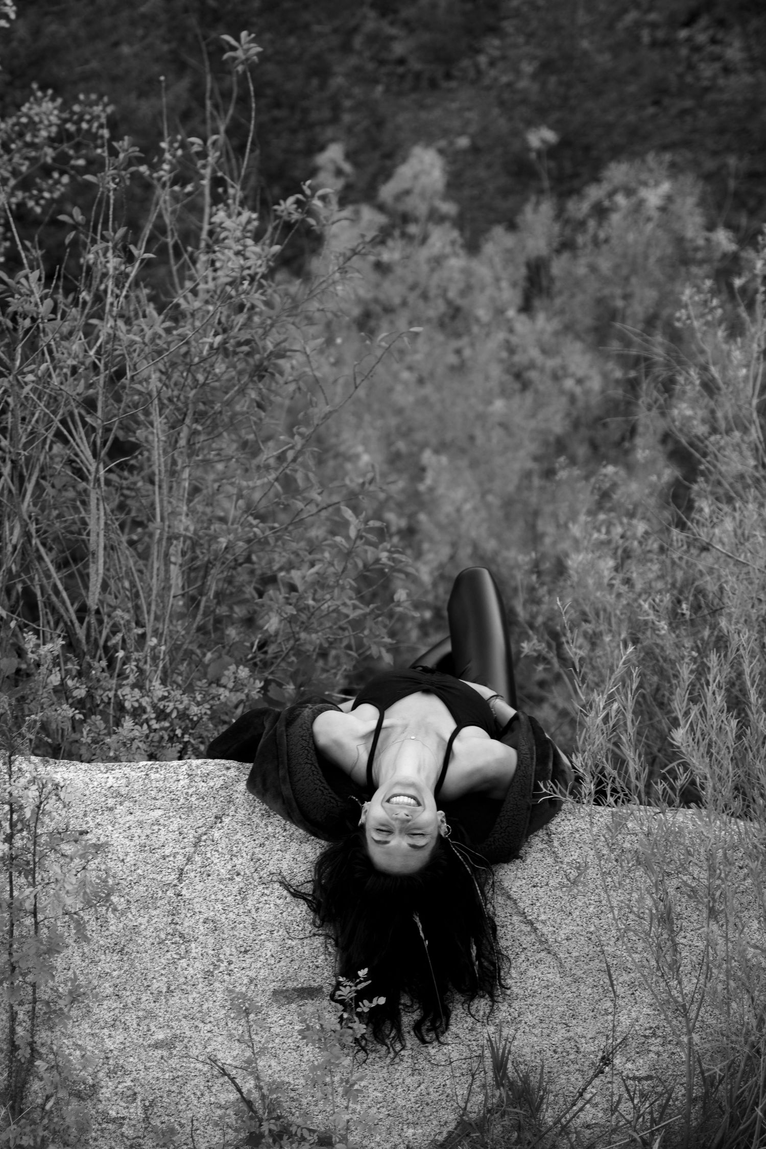 Artistic black and white photo of person reclining on concrete wall outdoors.