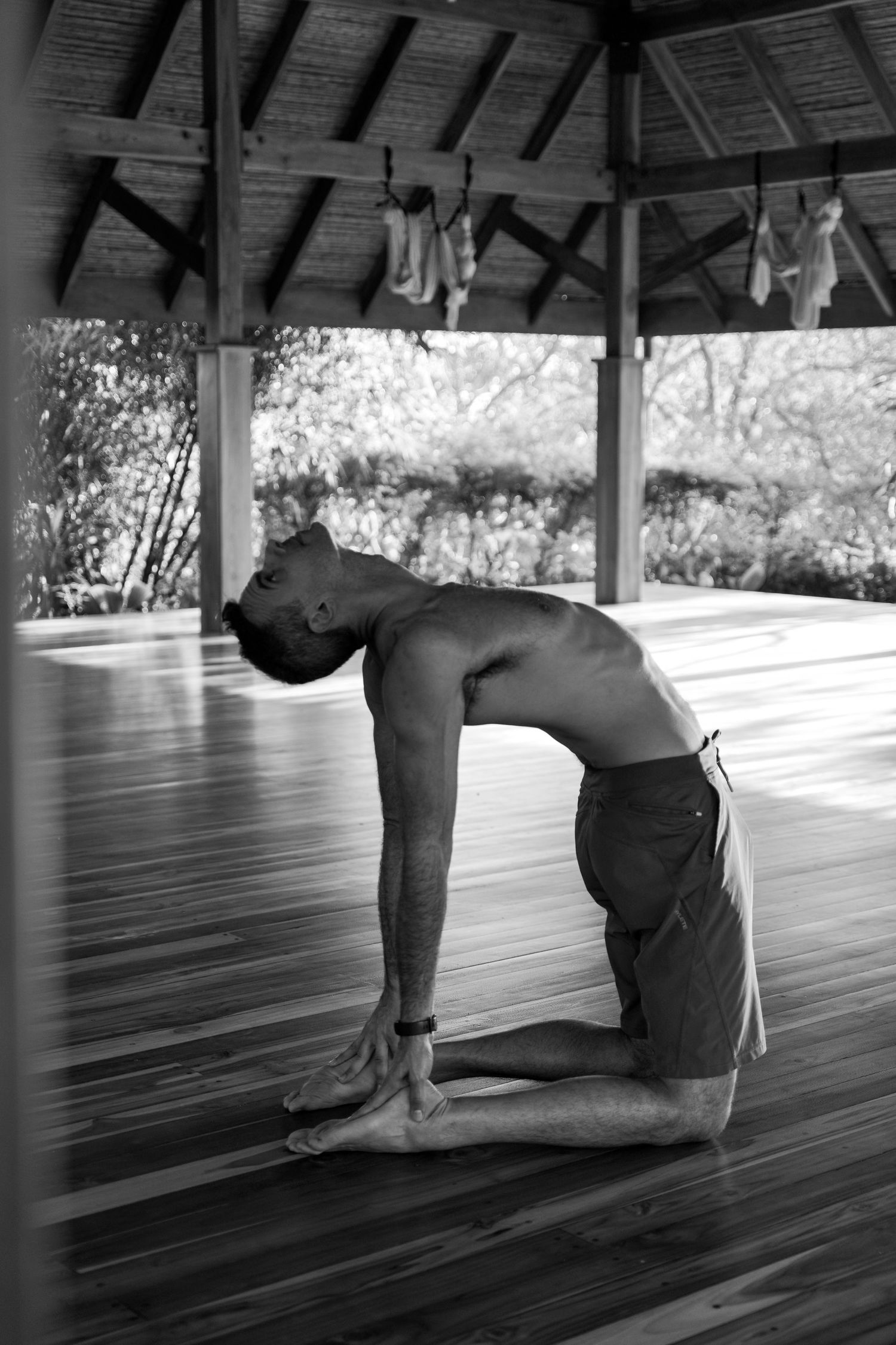 Black and white photo of person practicing yoga camel pose in wooden pavilion.