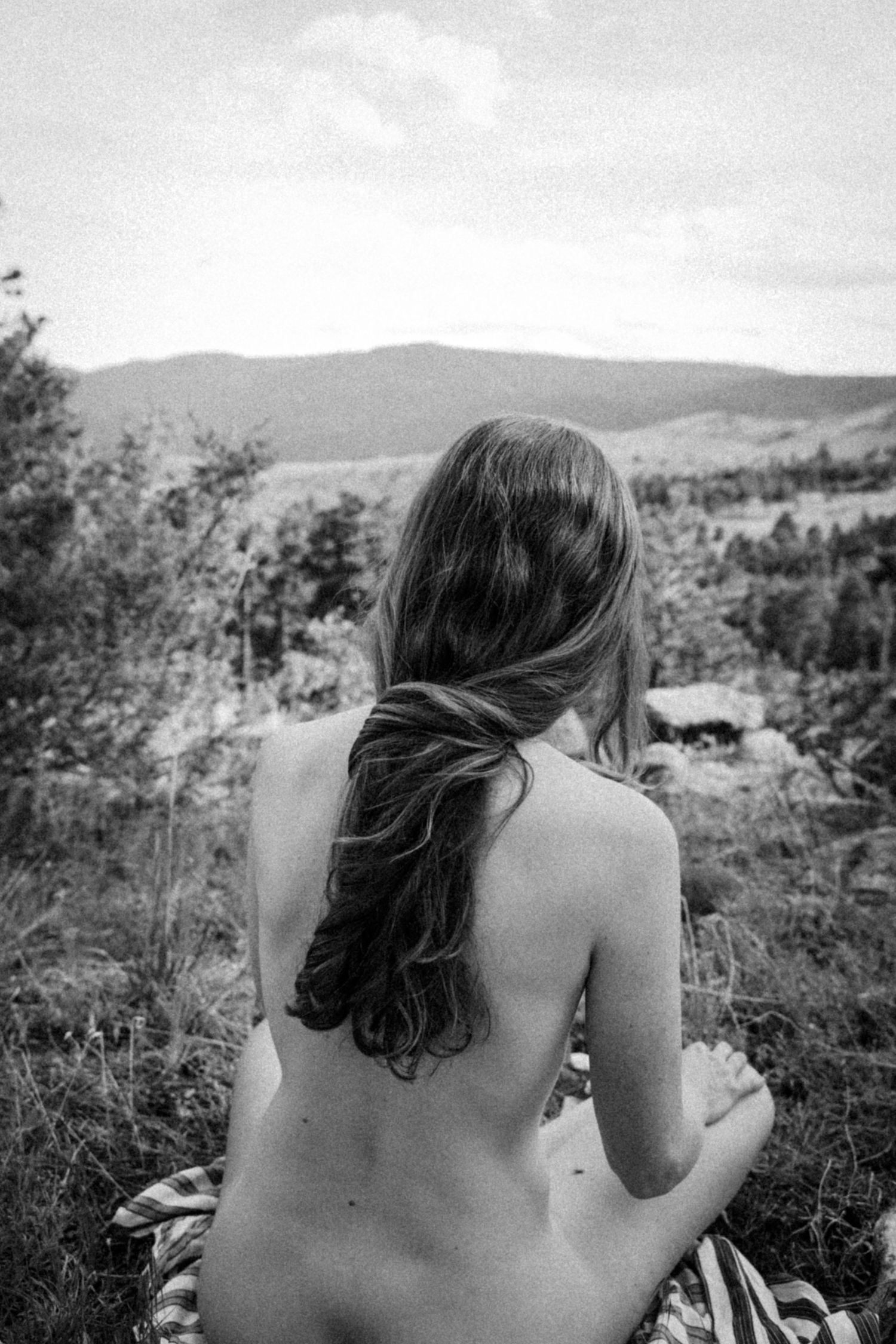 Black and white photo of long-haired figure overlooking mountain landscape.