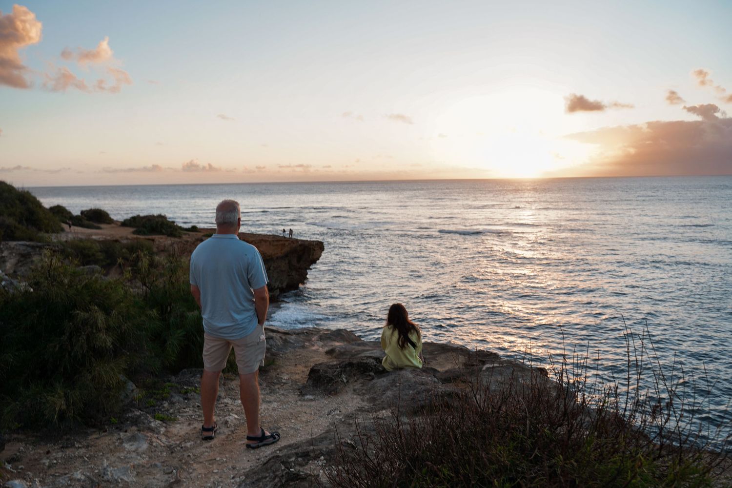 People watching sunset over ocean from scenic coastal cliff overlook.