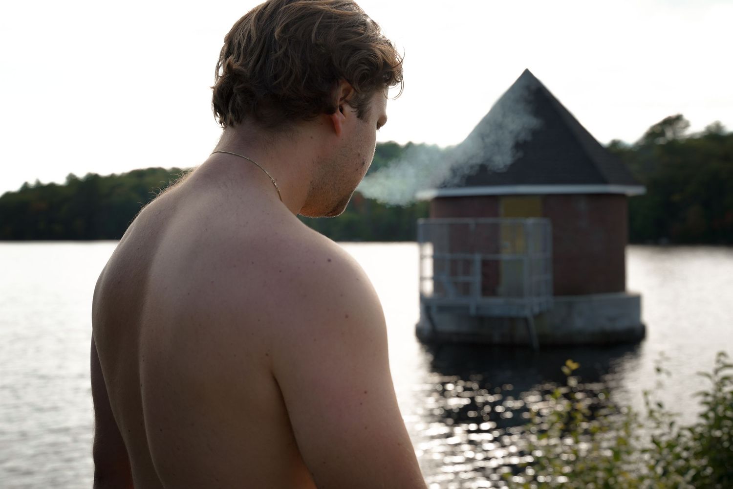 Person overlooking lake with floating boathouse at sunset.