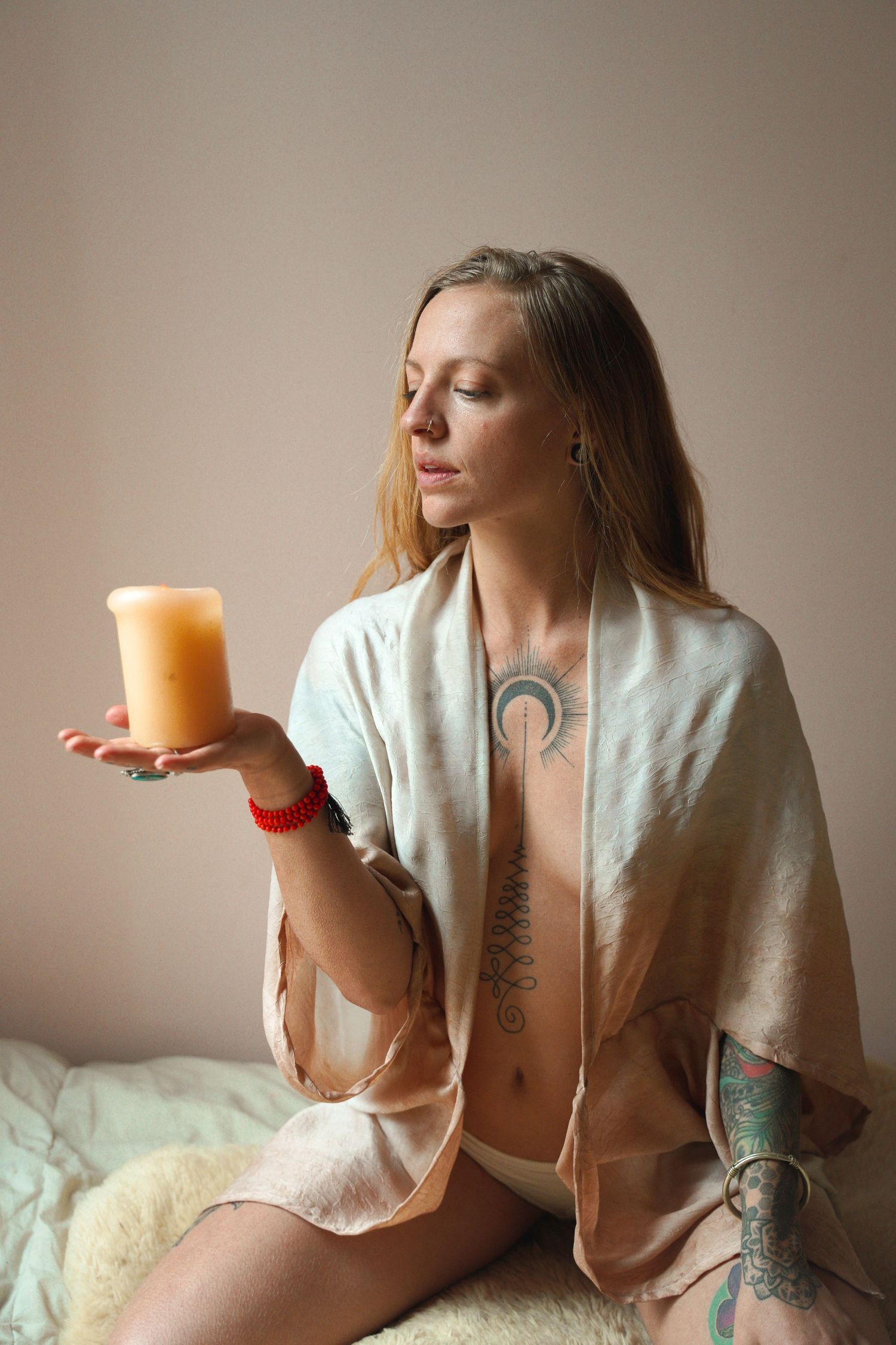 Person in robe holding orange candle with visible tattoos in minimalist portrait.