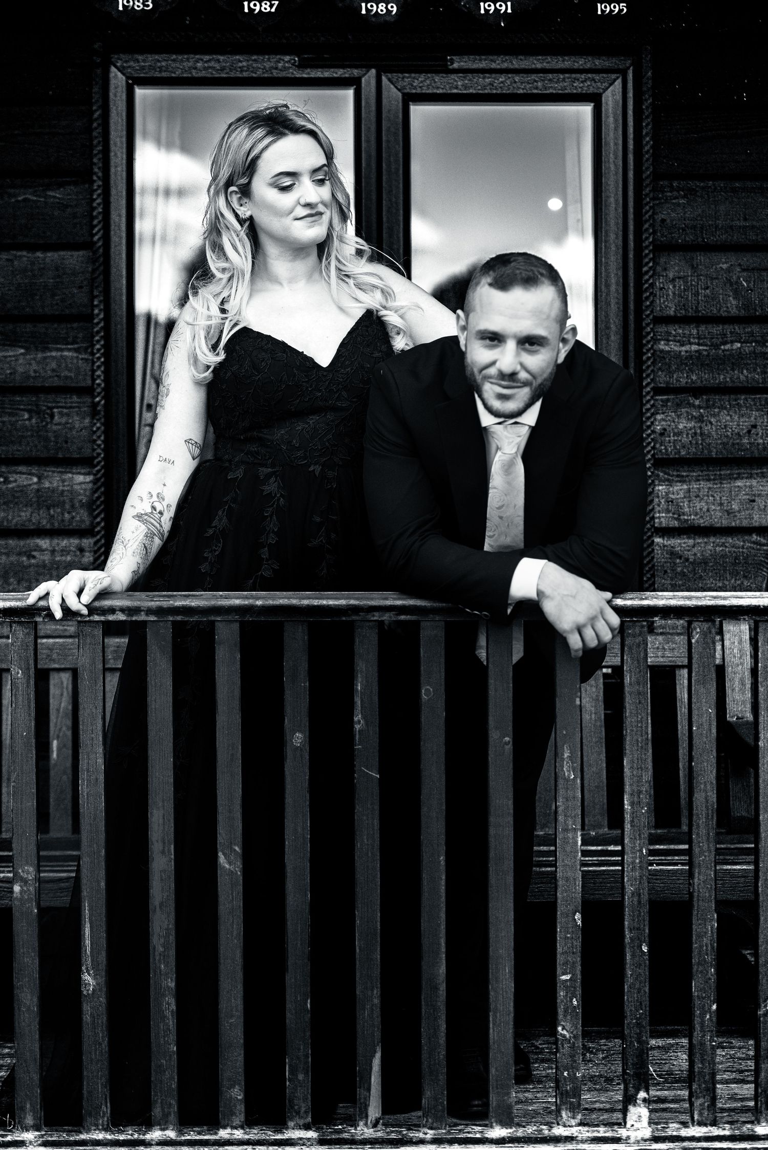 Black and white portrait of a couple posing together on a wooden balcony.