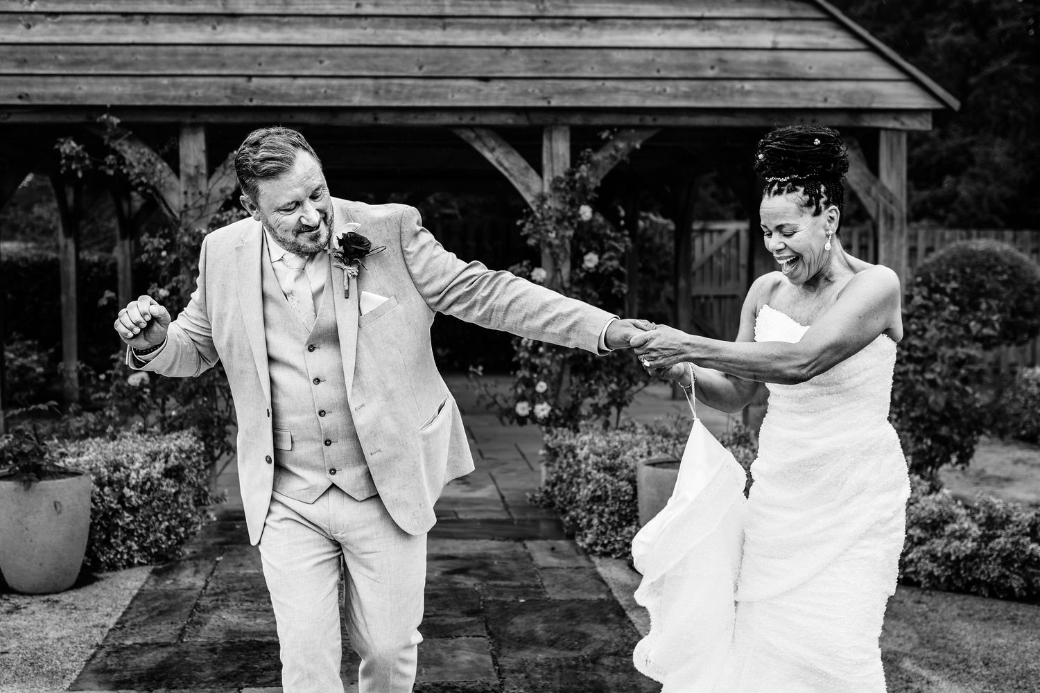 Joyful black and white wedding photograph of a bride and groom laughing while holding hands.