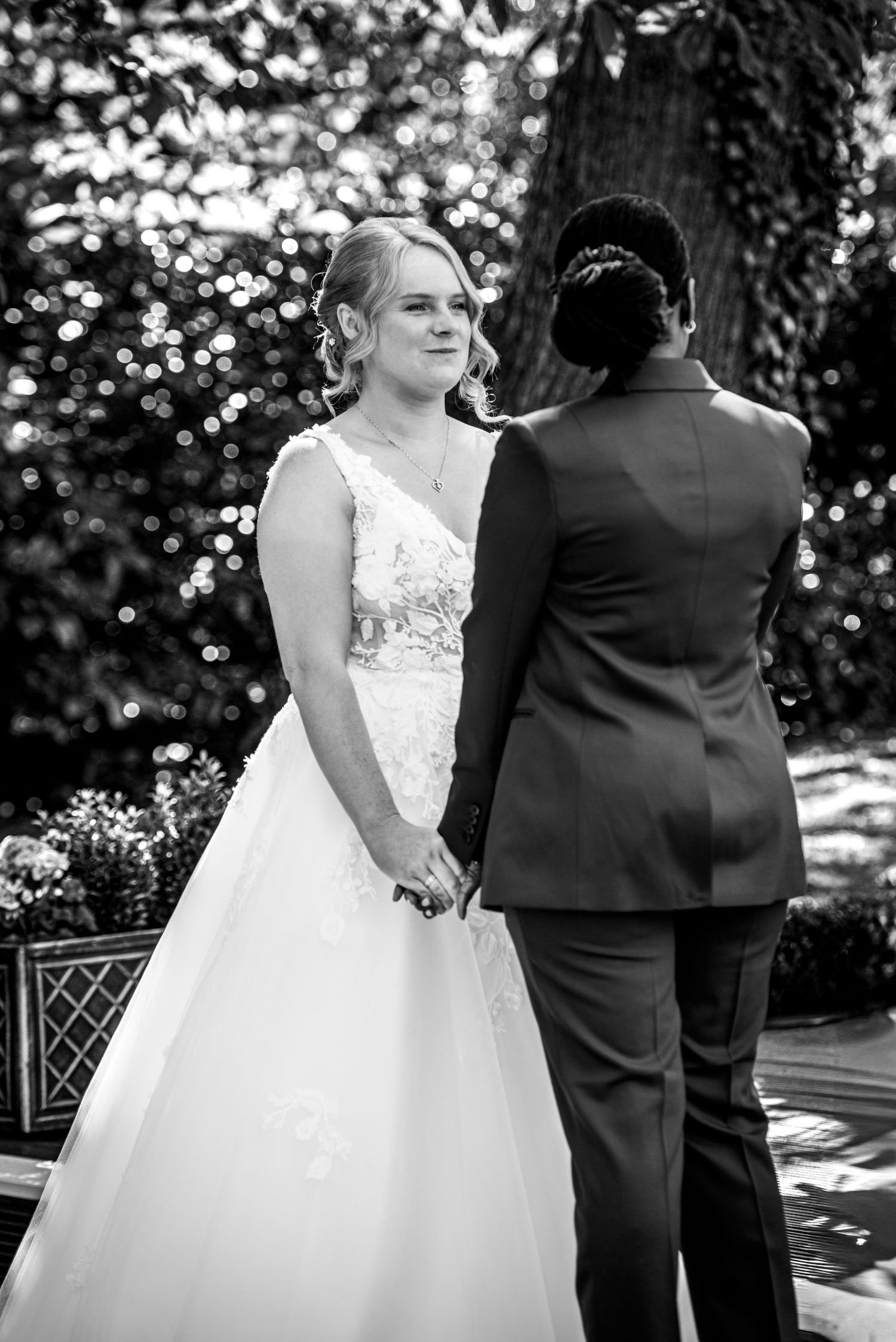 Black and white wedding photograph of a bride and groom holding hands beneath the trees.