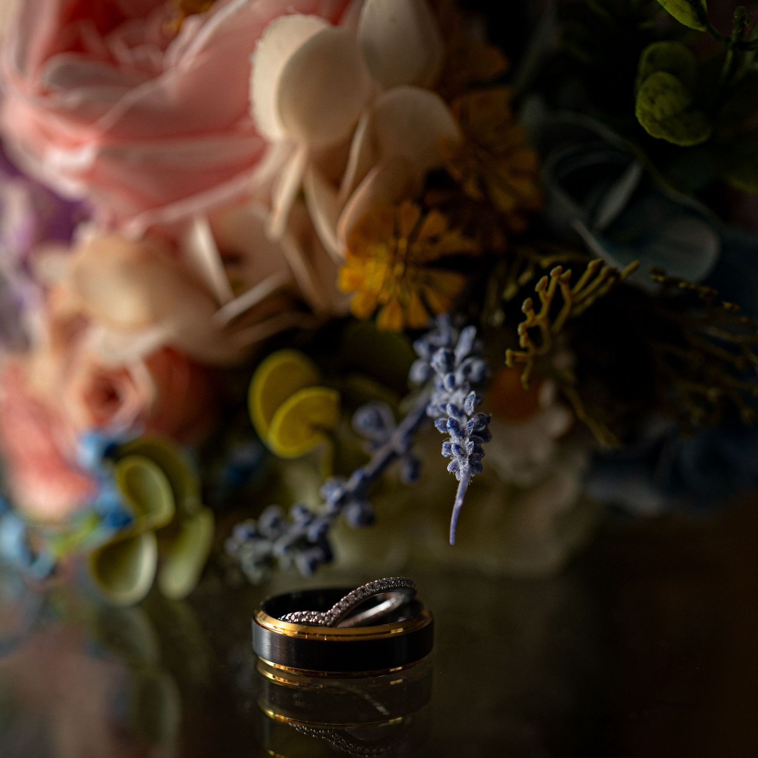 Artistic close-up of wedding rings surrounded by softly lit flowers.