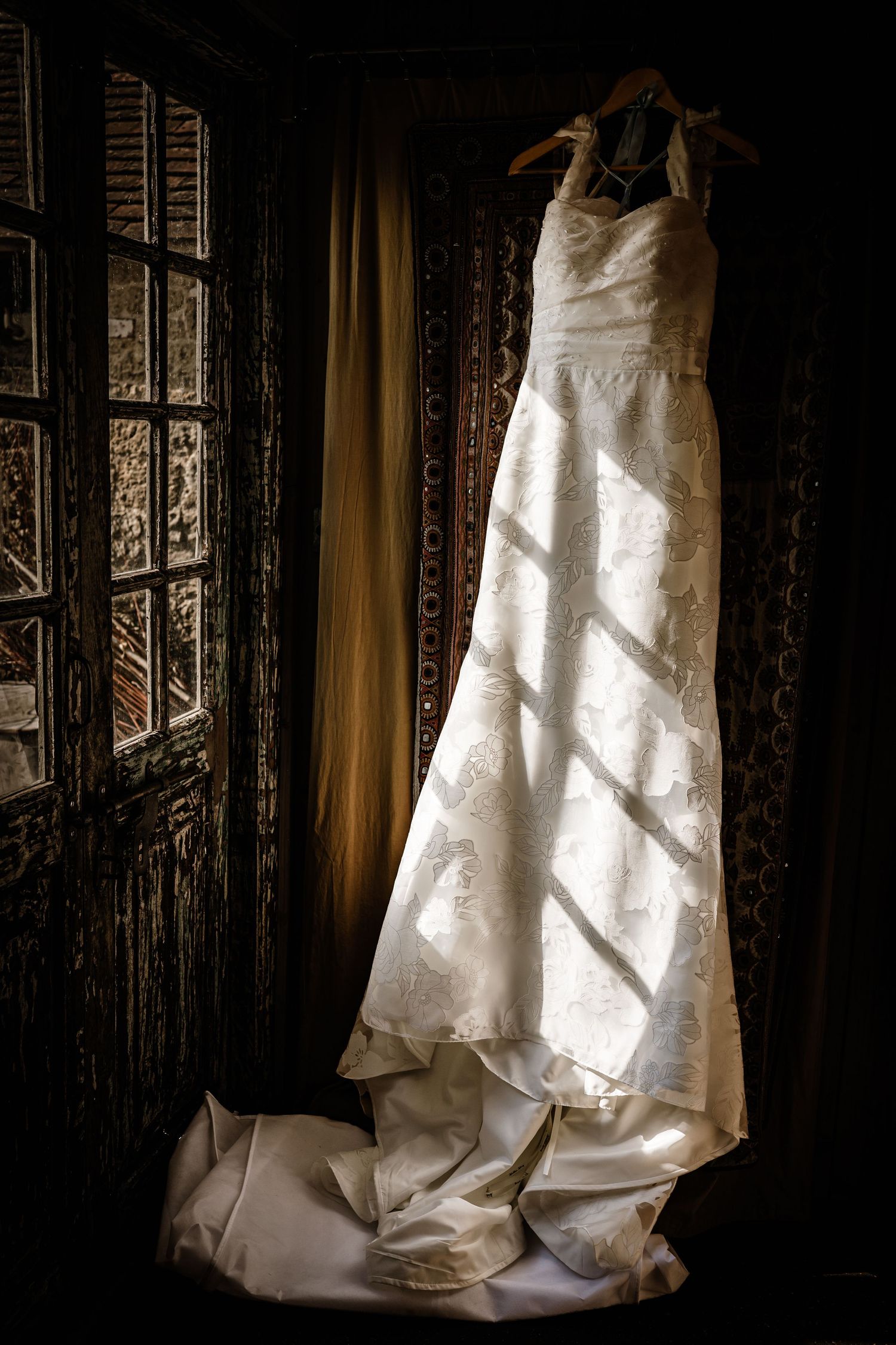 Elegant wedding dress hanging beside a window in soft natural light.
