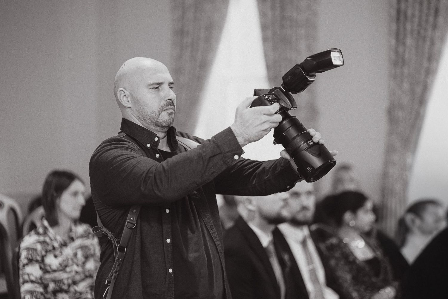 Black and white behind-the-scenes photograph of a wedding photographer taking pictures during a ceremony.
