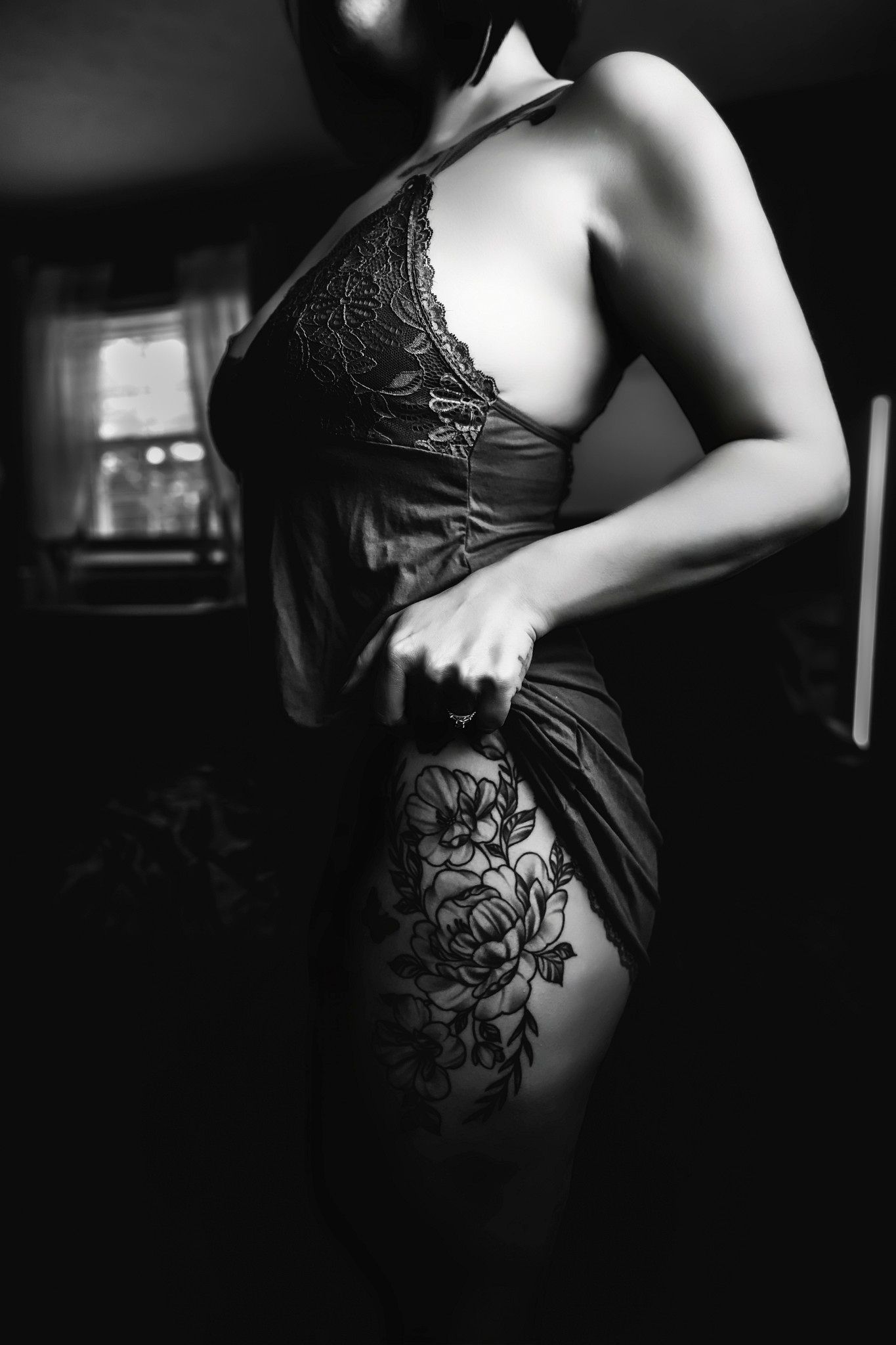 Black and white boudoir photo of a woman in lace lingerie with floral thigh tattoo, artistic moody lighting.