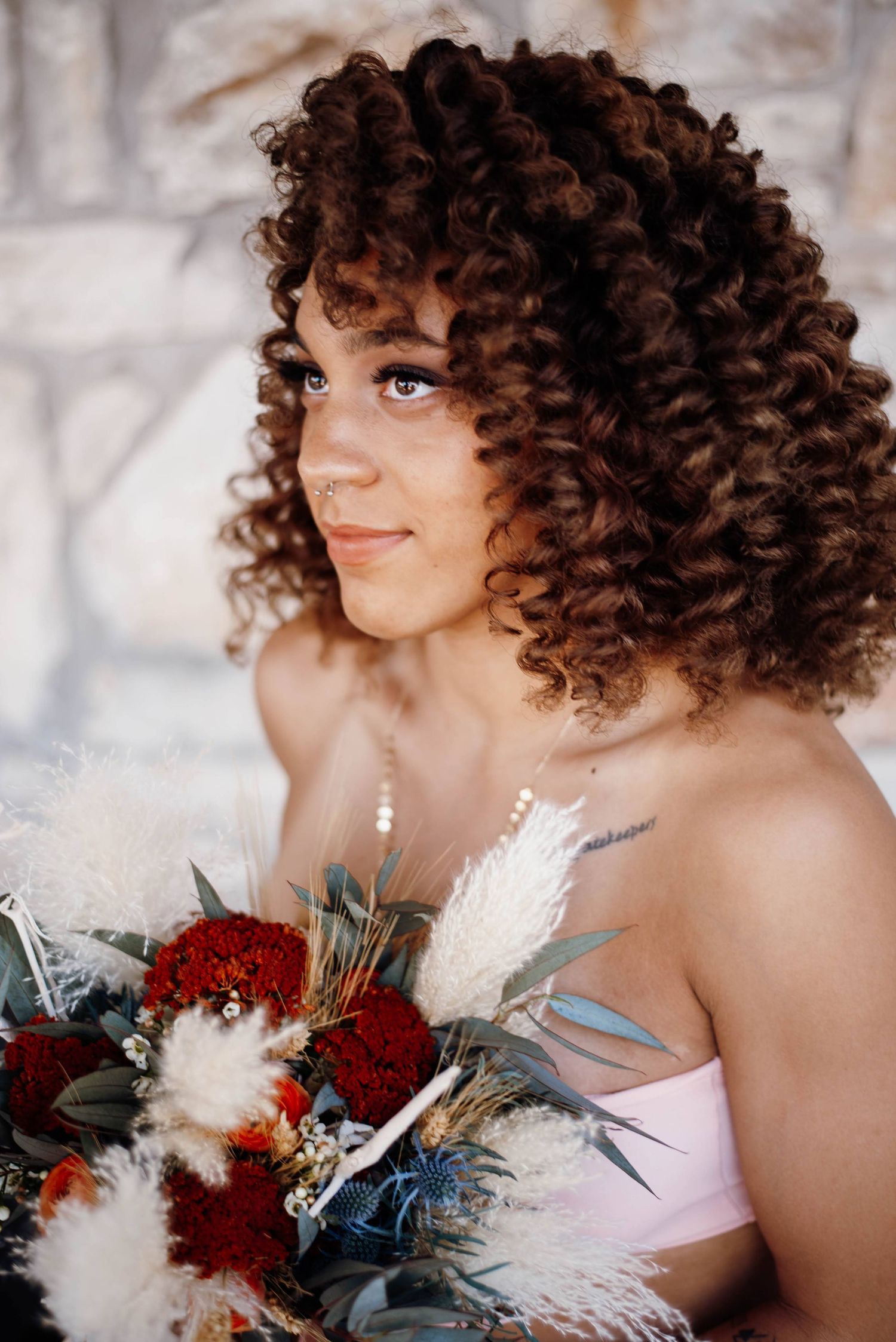 Young woman with curly auburn hair holding a boho floral bouquet with red and white flowers.