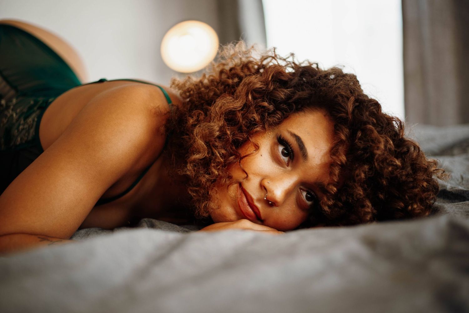 Woman with curly hair lying on a bed wearing green lingerie with a soft smile.