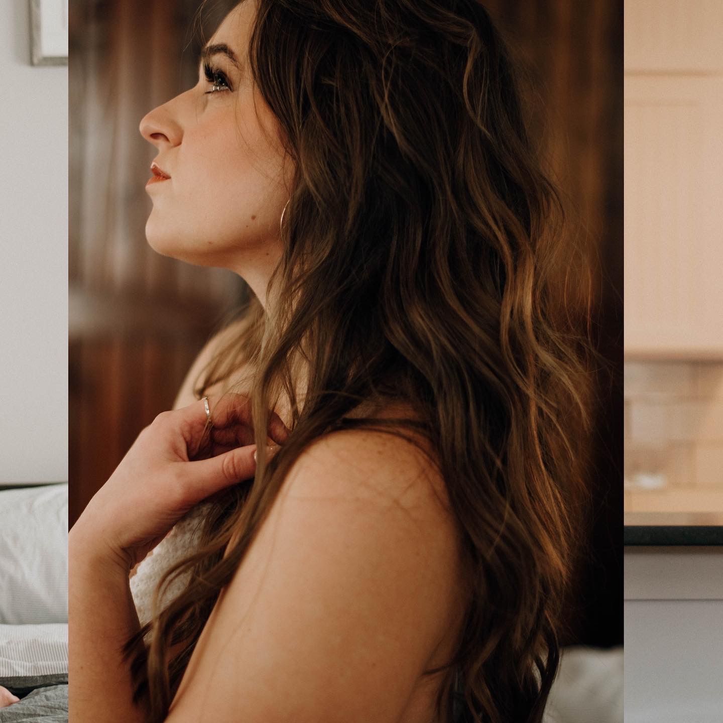 A woman with long wavy brunette hair poses in profile view, looking upward in soft natural light.