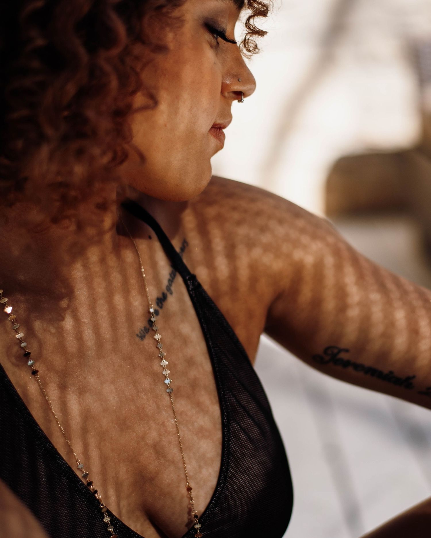 Woman with curly red hair wearing black halter top and layered necklaces, with tattoo visible on arm.
