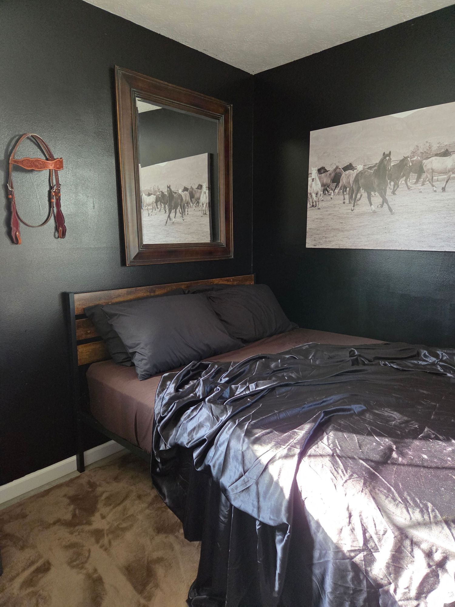 Dark western bedroom with black walls, horse art prints, rustic mirror, and charcoal satin bedding on a wood bed frame.