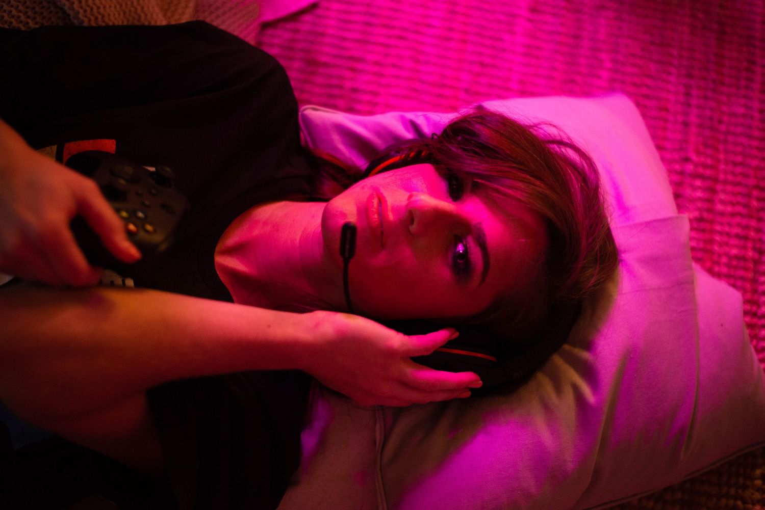 Woman lying on a pillow with a hand near her face under moody pink neon lighting indoors.