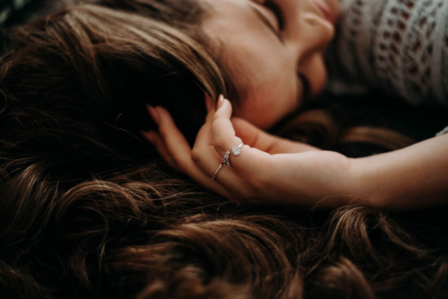 Close-up of a child's hand resting on a woman's long brown hair, wearing a delicate ring.