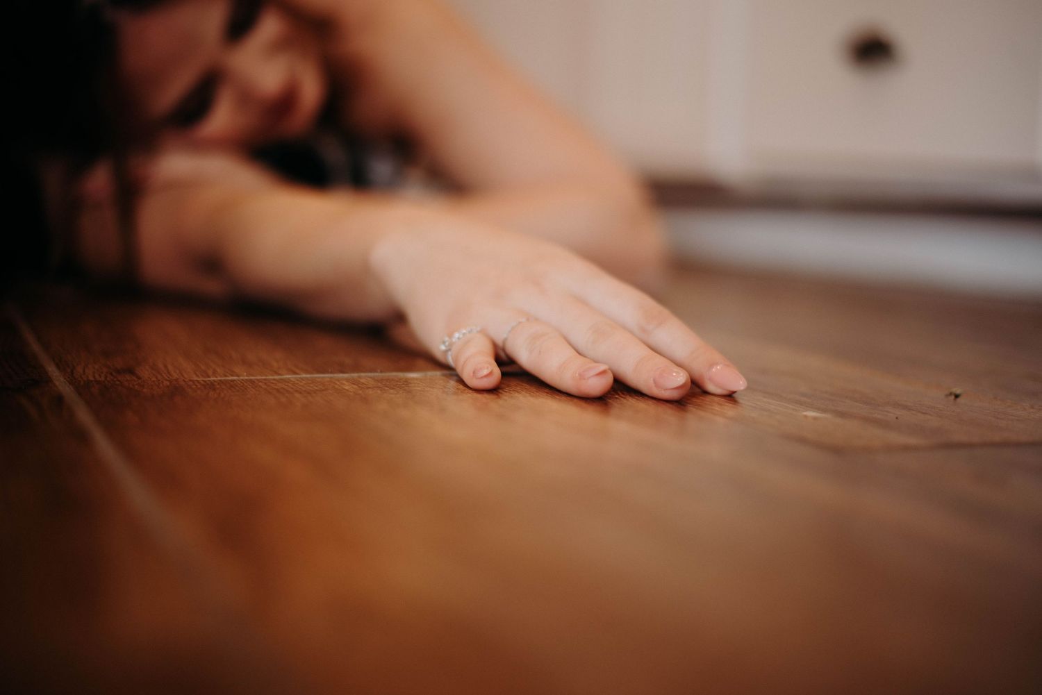 Woman lying on hardwood floor with hand outstretched, close-up of wooden floor texture.