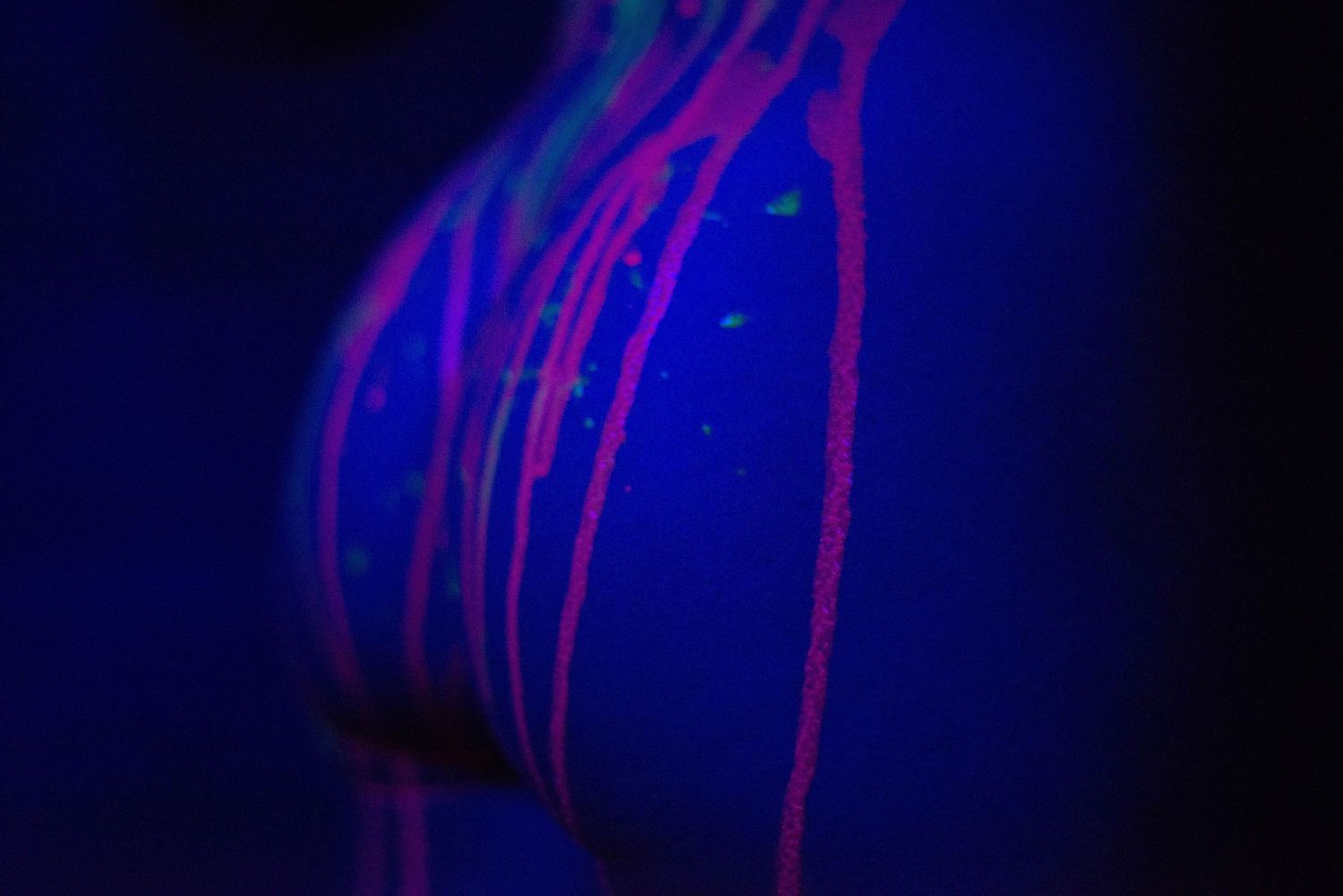 Abstract body art glowing under UV black light with vibrant pink and green neon paint streaks on skin.