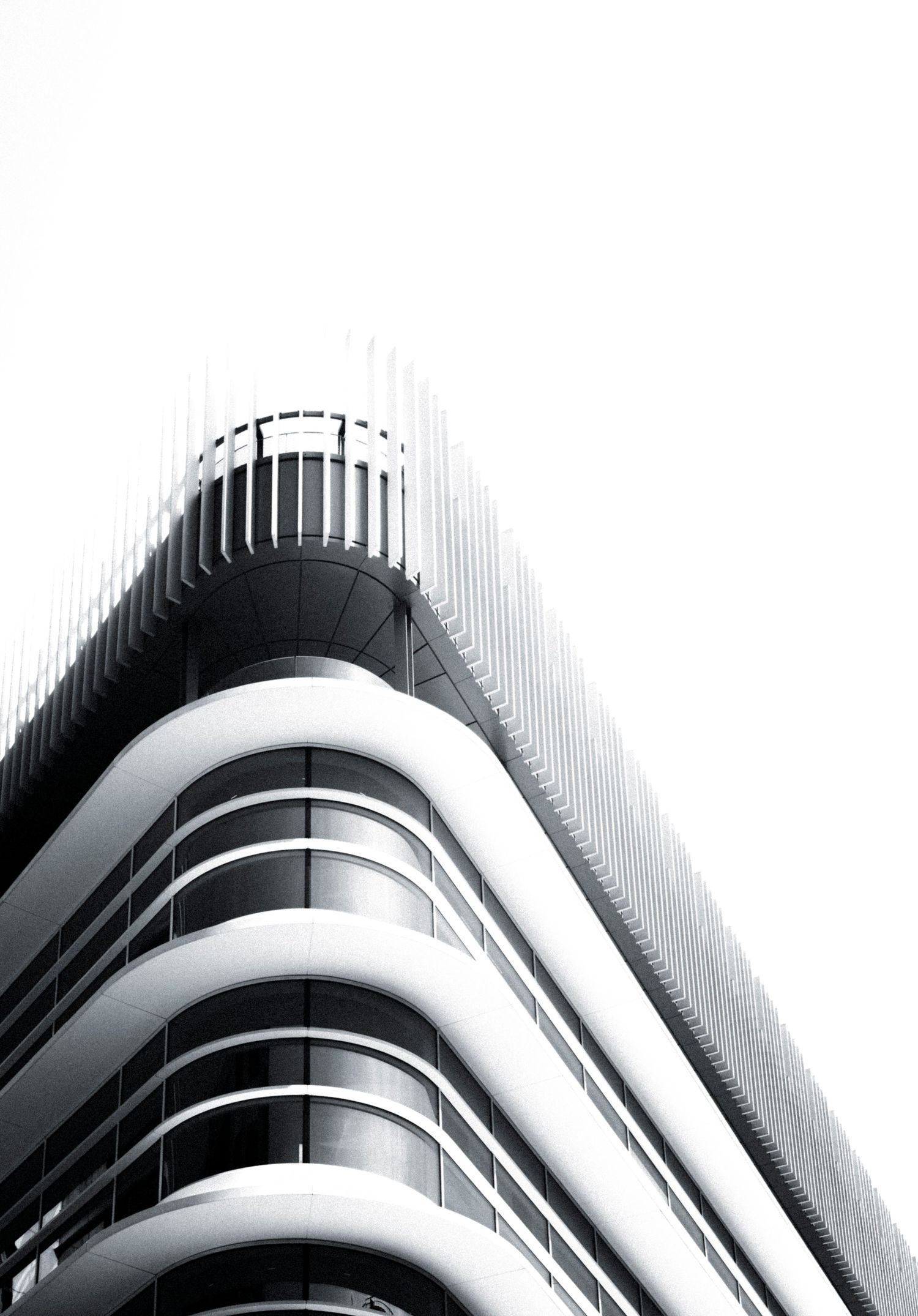 Black and white low-angle shot of a modern curved glass skyscraper facade disappearing into a white sky.