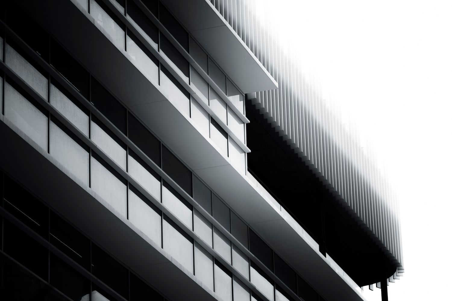 Black and white architectural photo of a modern glass office building facade with sleek lines and balconies.