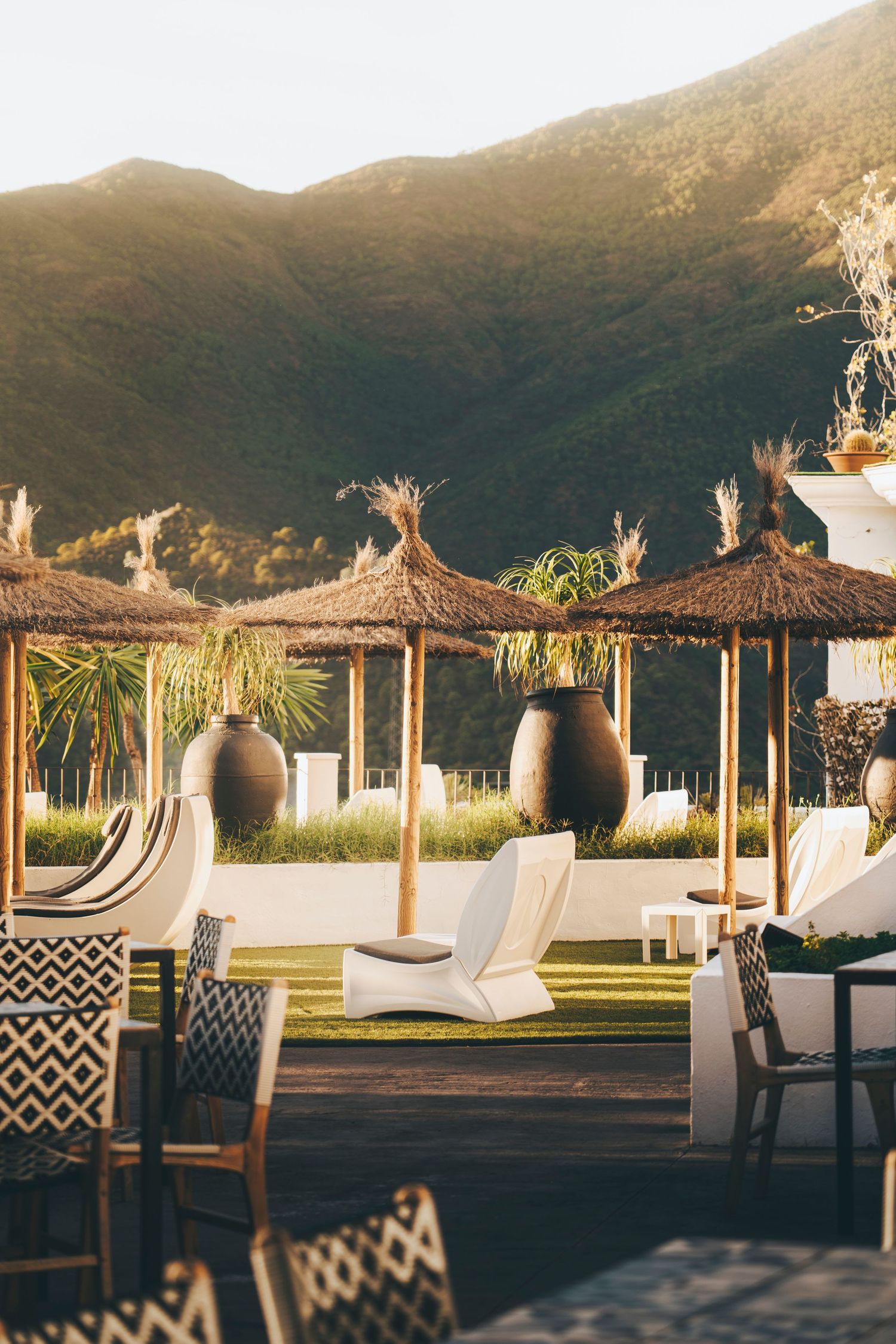 Luxury outdoor terrace with thatched umbrellas, white lounge chairs, and stunning mountain backdrop at golden hour.