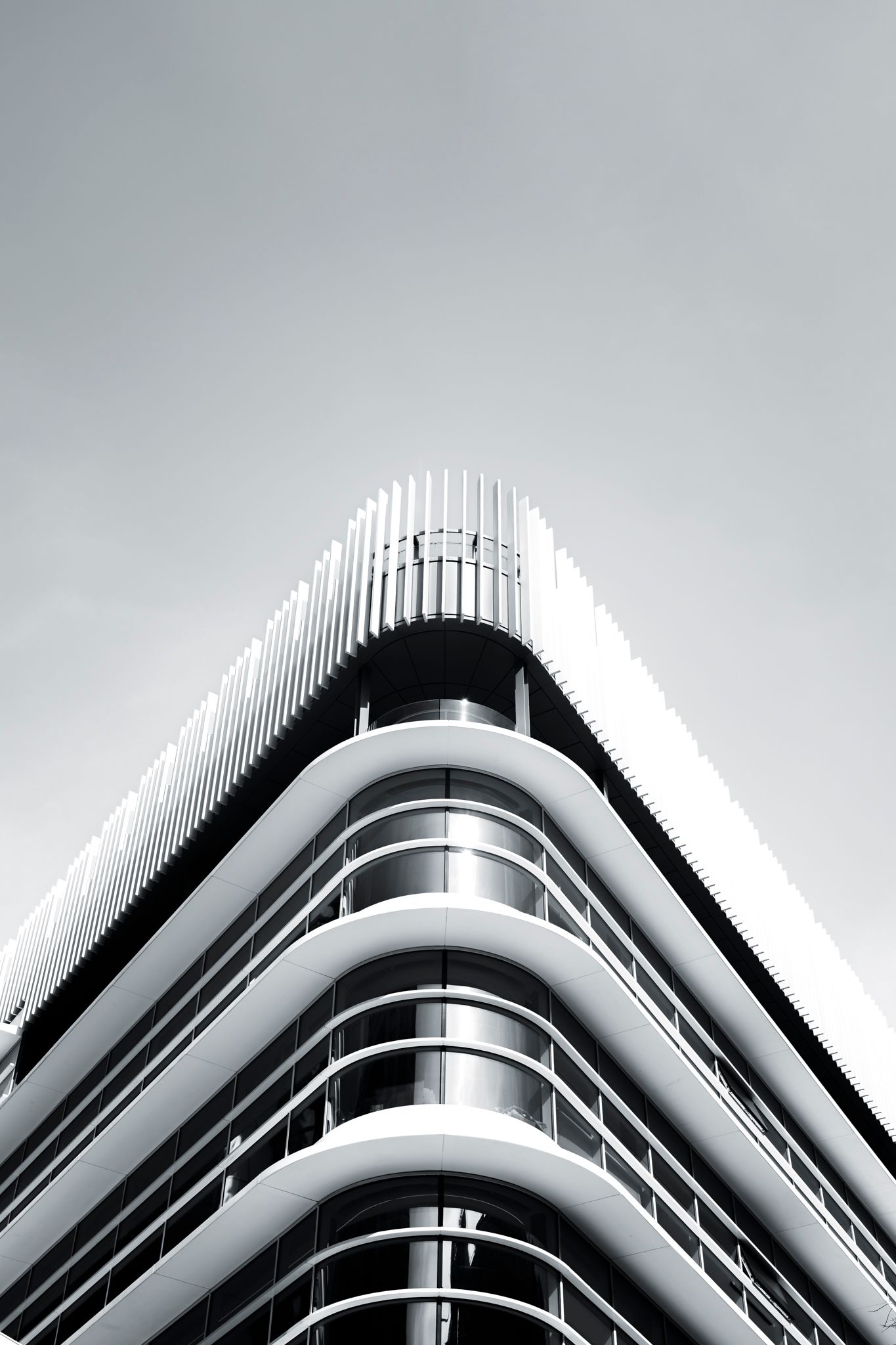 Low angle black and white view of a modern curved white building facade against overcast sky.
