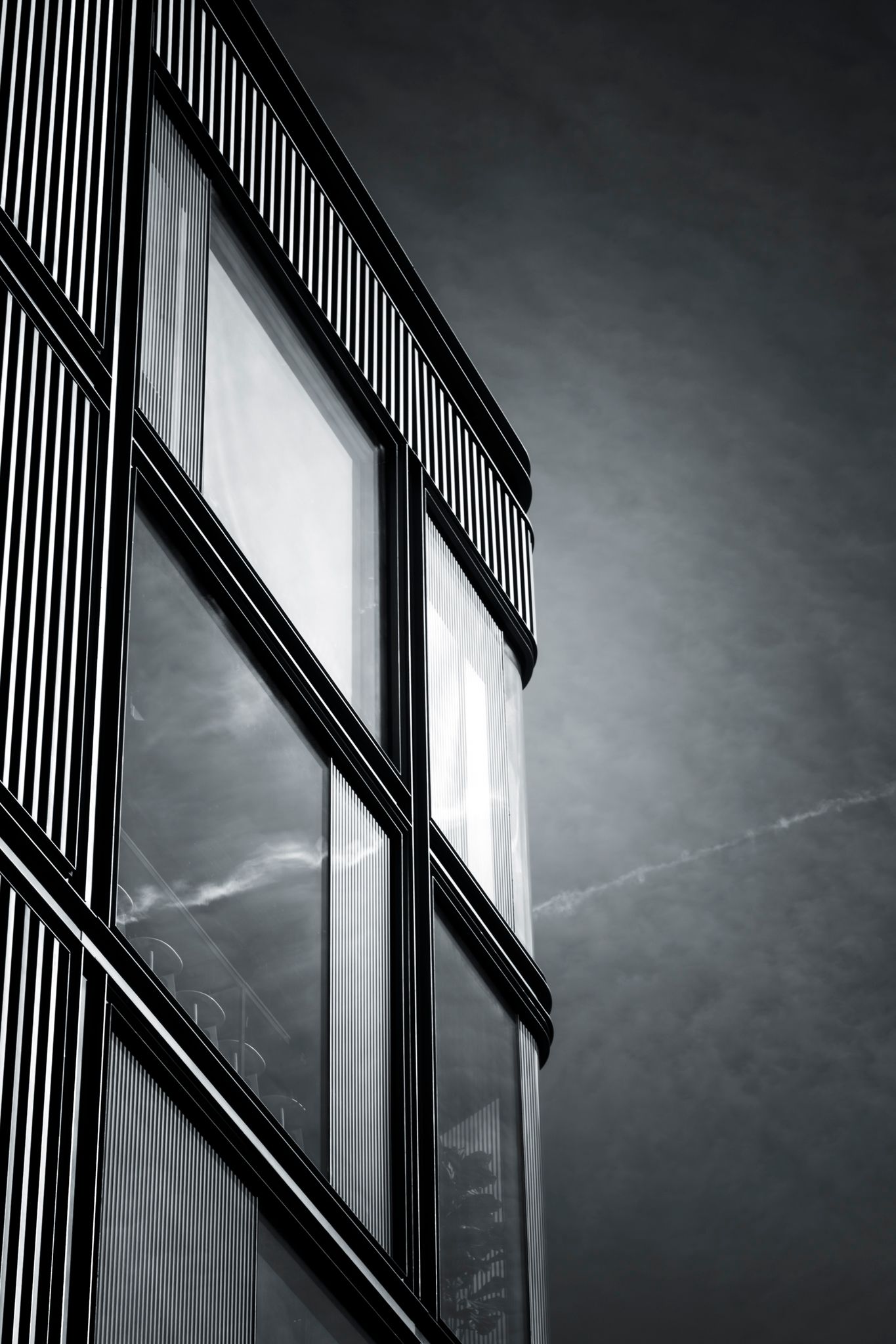 Black and white close-up of a modern glass corner building with vertical fins under a dramatic cloudy sky.