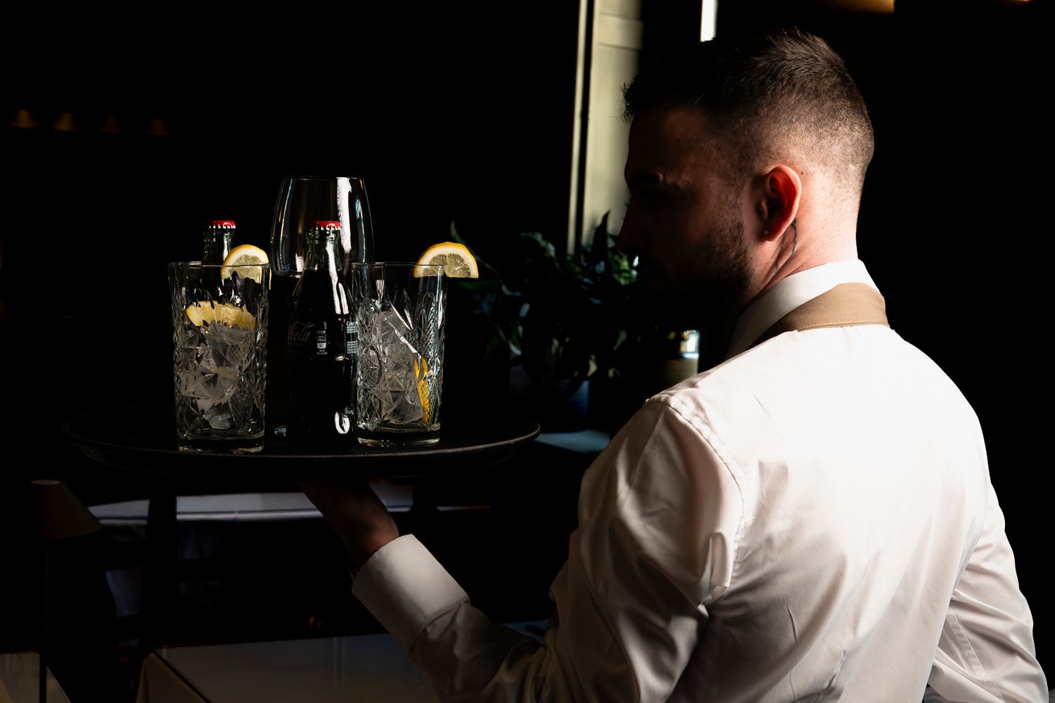 Waiter in white shirt carrying a tray of elegant cocktails with lemon garnishes at a formal event.