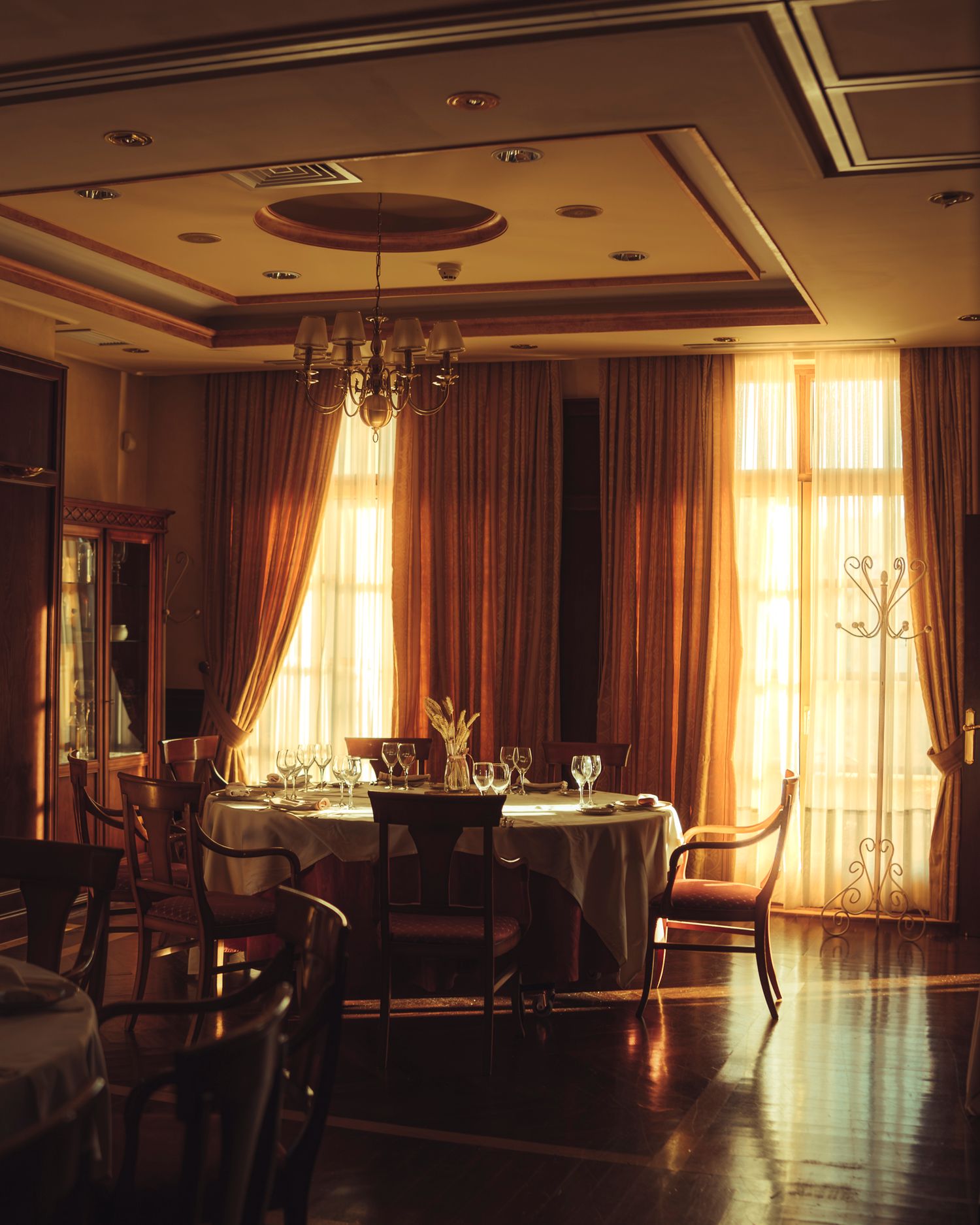 Upscale restaurant dining room with chandelier, round tables, wine glasses, and warm golden curtains.
