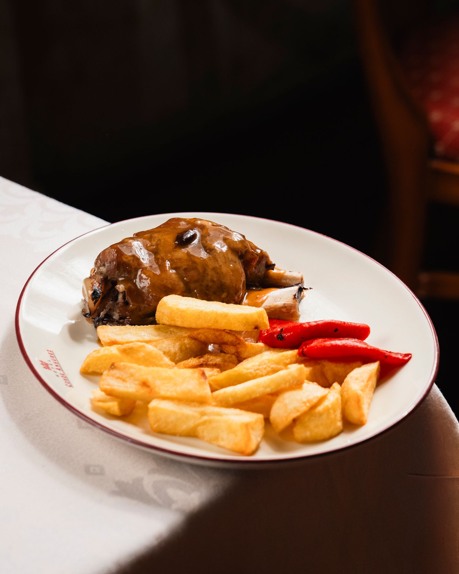 Braised meat with thick-cut fries and red peppers on a white plate with red trim.