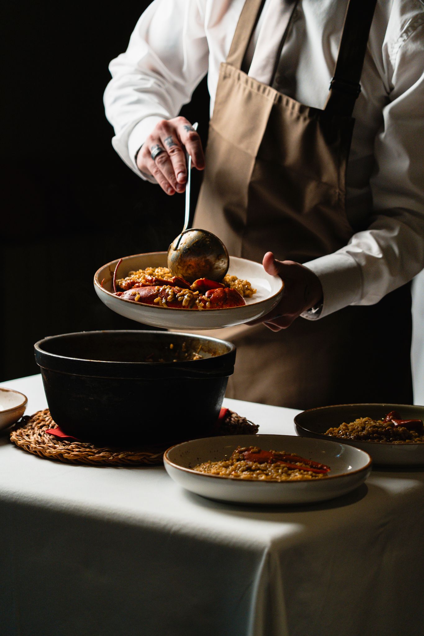 Chef serving aromatic rice and seafood dish from a large black pot onto a white plate.