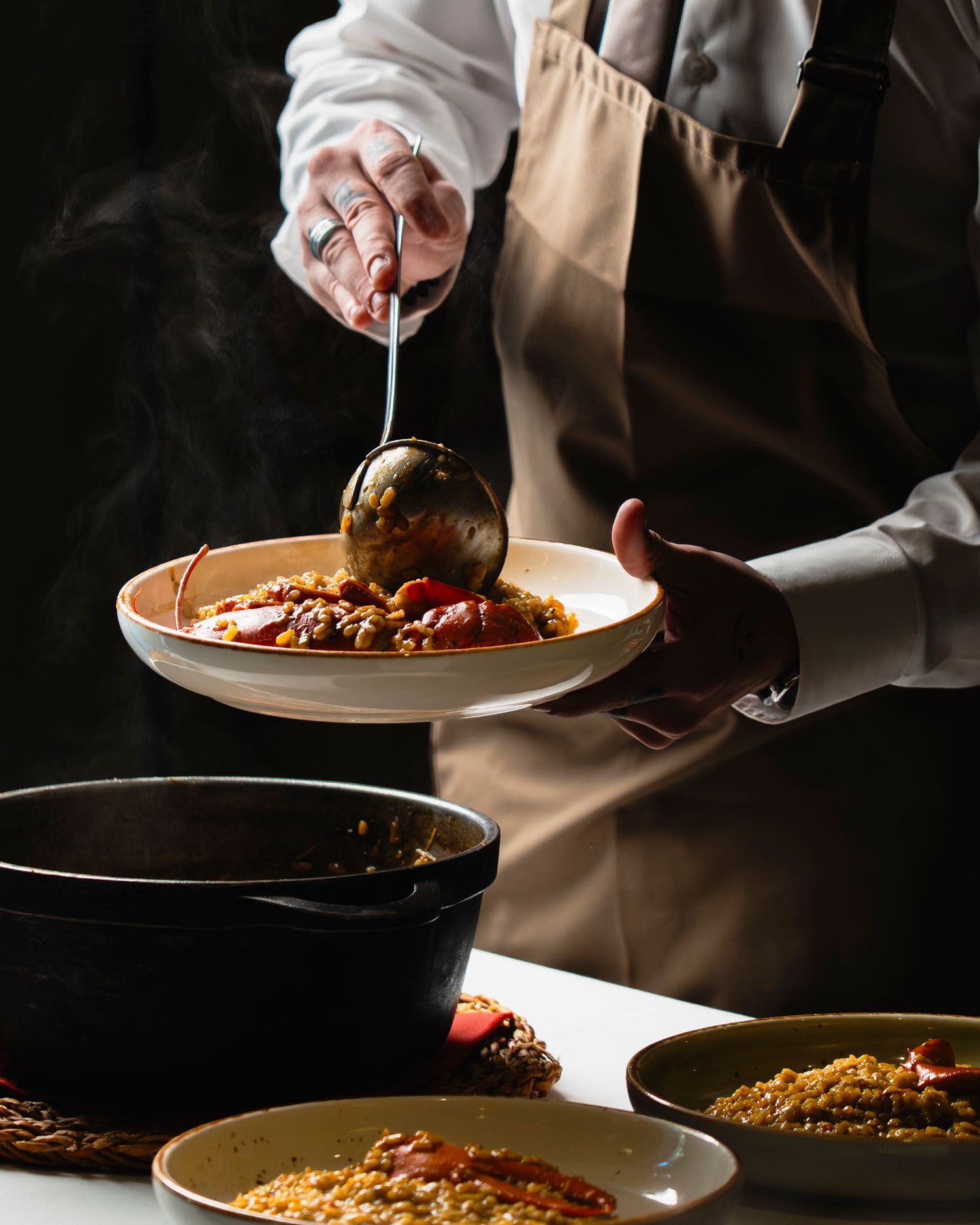 Chef ladling steaming hot stew onto a ceramic plate at a fine dining restaurant.