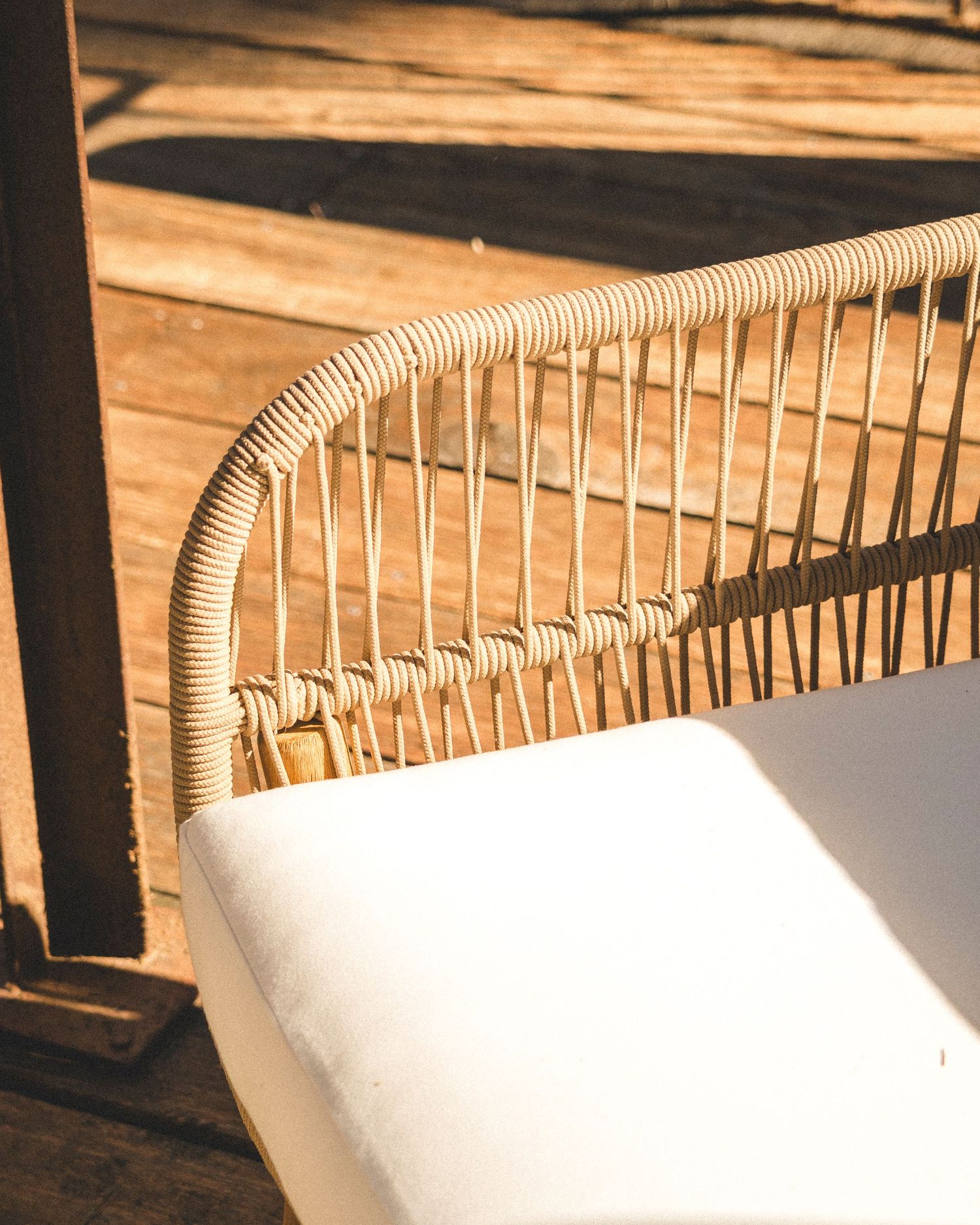 Close-up of a woven rattan outdoor chair with white cushion on a wooden deck.