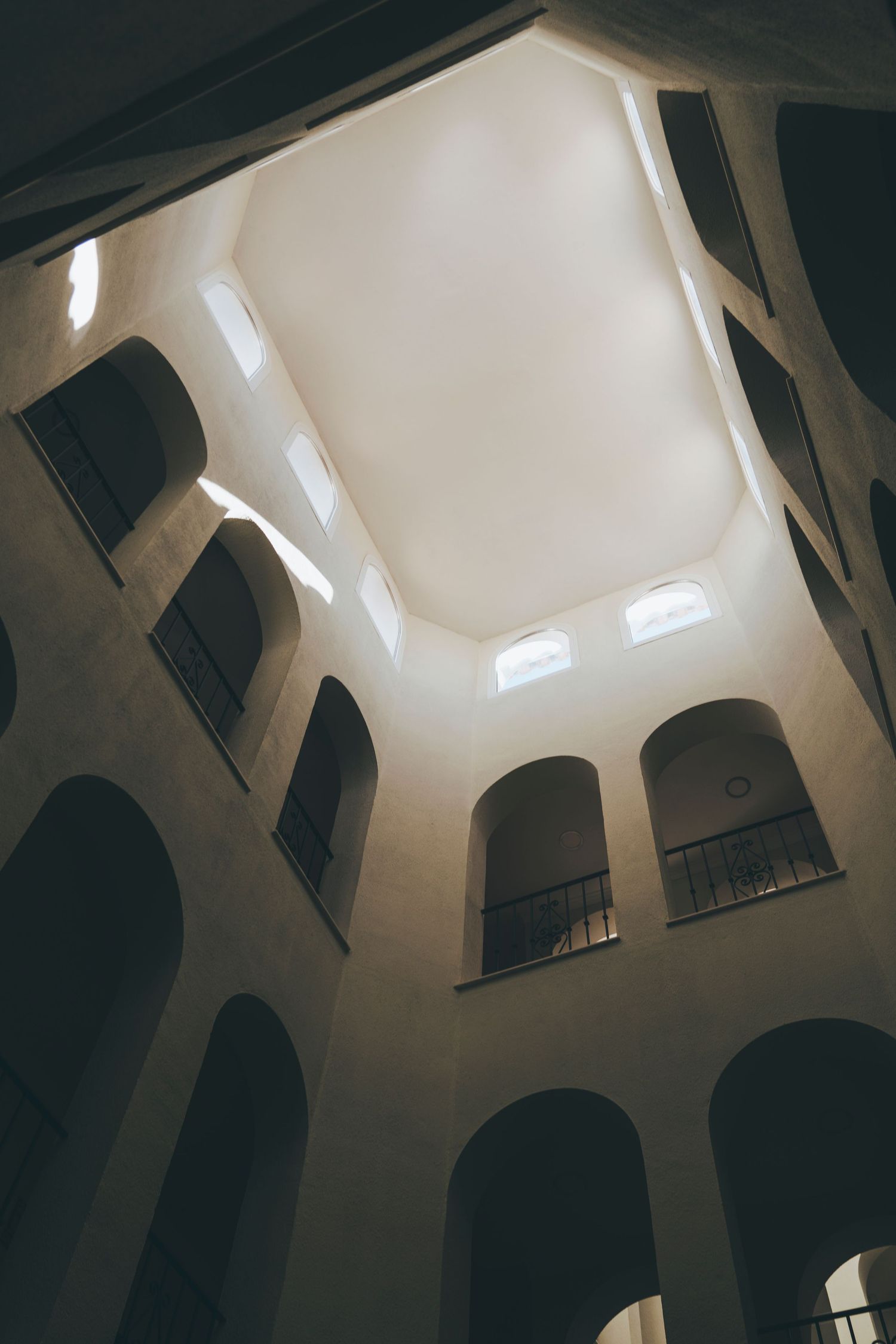 Dramatic interior atrium view looking up at octagonal skylight through arched windows and balconies in historic building.
