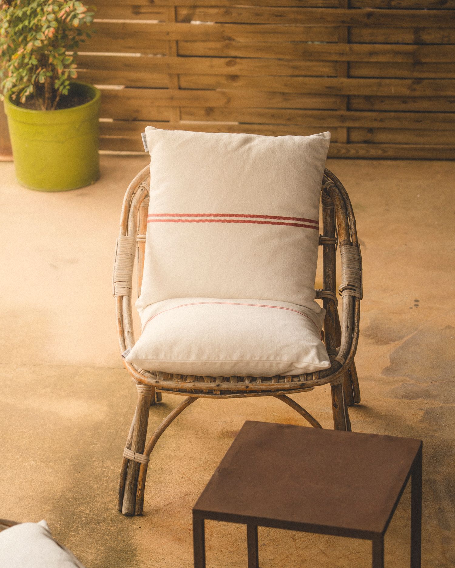 Rattan chair with white striped cushion beside a small wooden table on a warm outdoor terrace patio.
