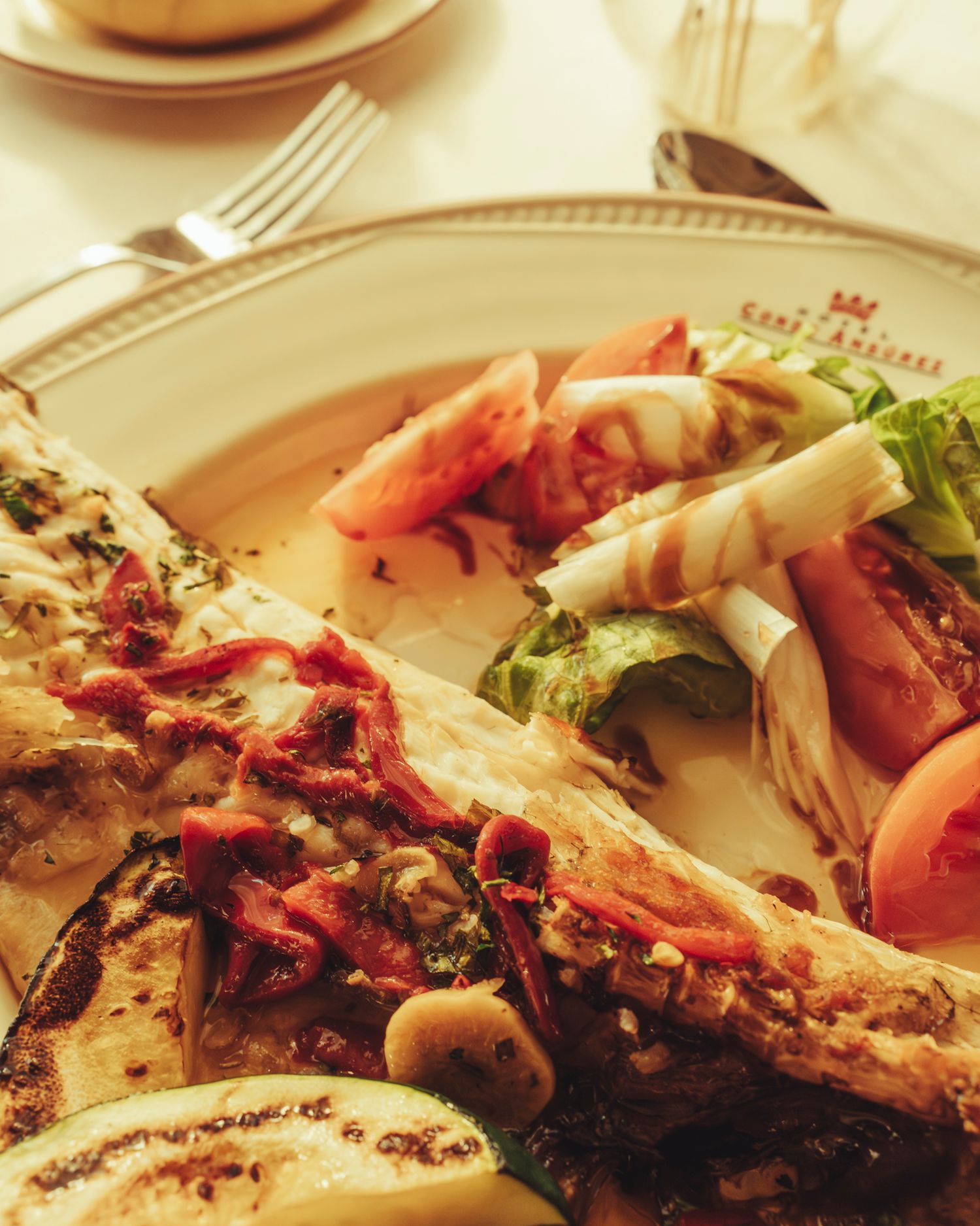 A grilled fish fillet with fresh salad and tomatoes on a white restaurant plate.