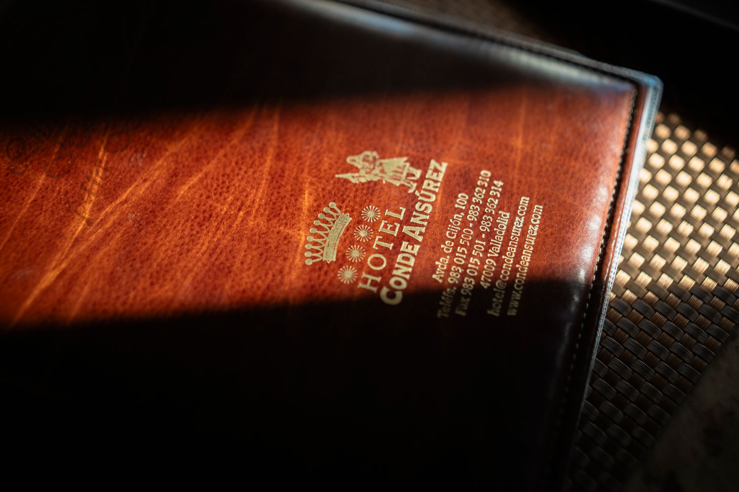 Close-up of an embossed leather Hotel Conde Ansуrez menu cover with gold lettering in warm brown tones.