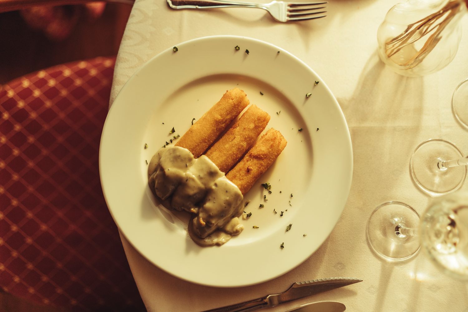 Three golden fried crepes topped with creamy mushroom sauce on a white plate at an elegant restaurant.