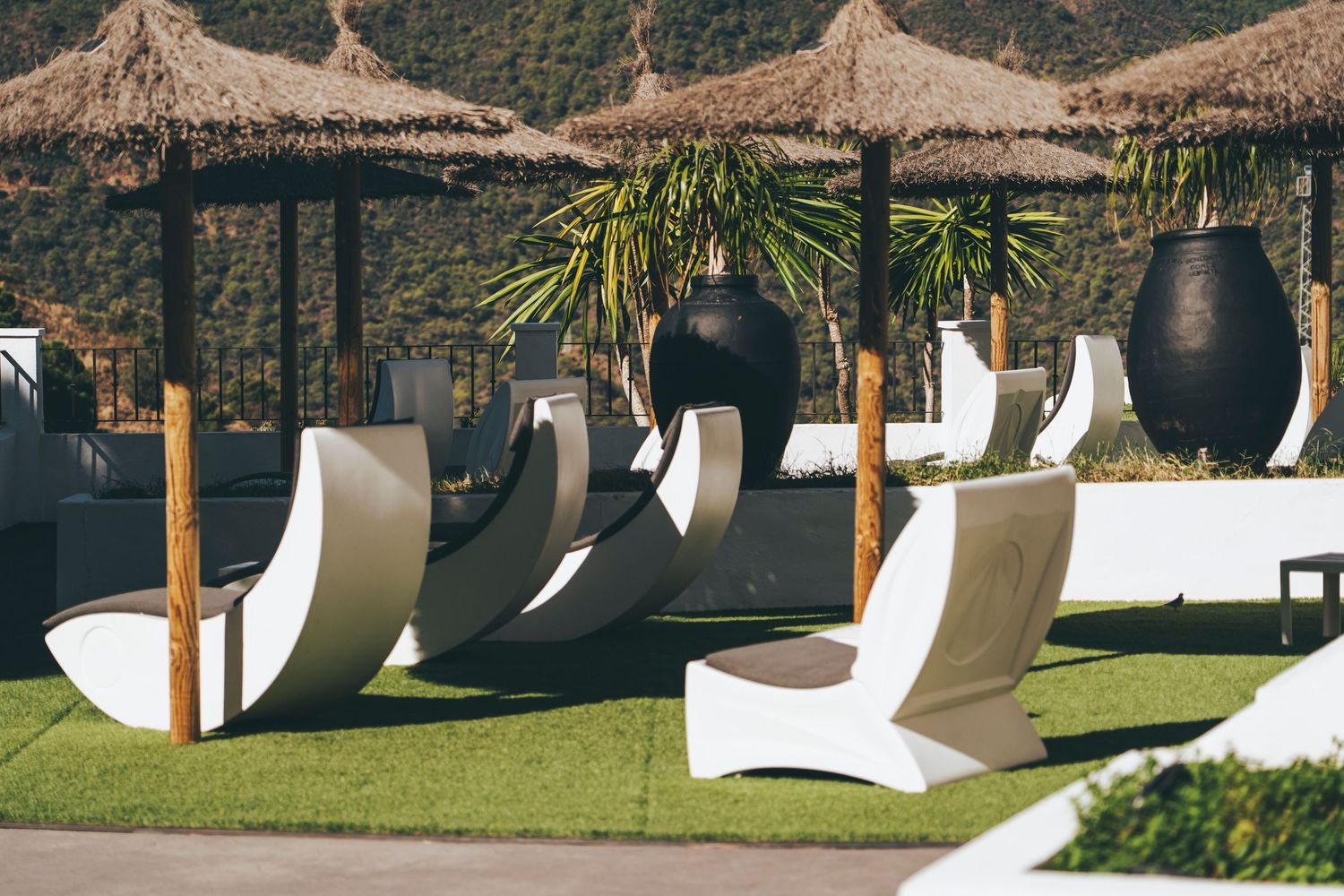 Modern white lounge chairs and thatched umbrellas on a green lawn at a luxury resort pool area.