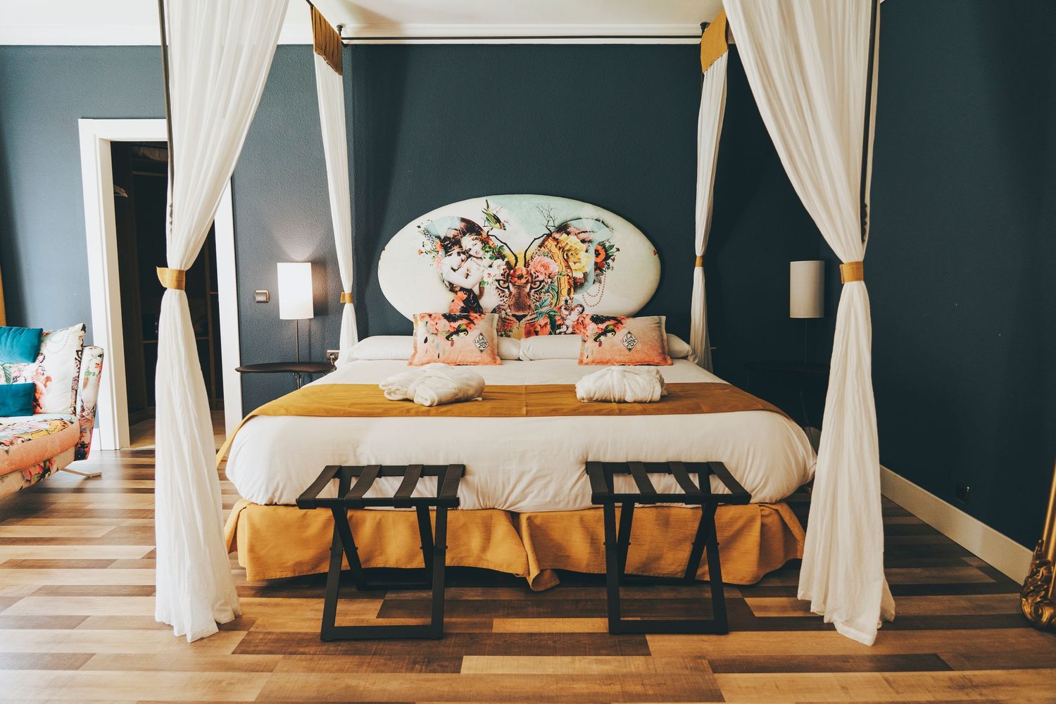 Luxury four-poster bed with white canopy drapes, yellow bedding, and floral headboard in a boutique hotel room.