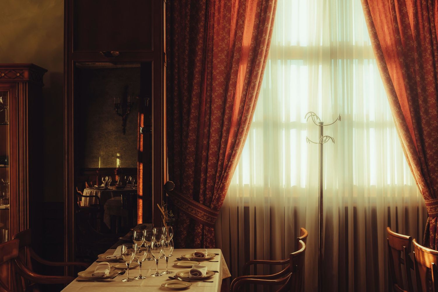Elegant restaurant dining room with red drapes, candlelight, and a formally set table for two.