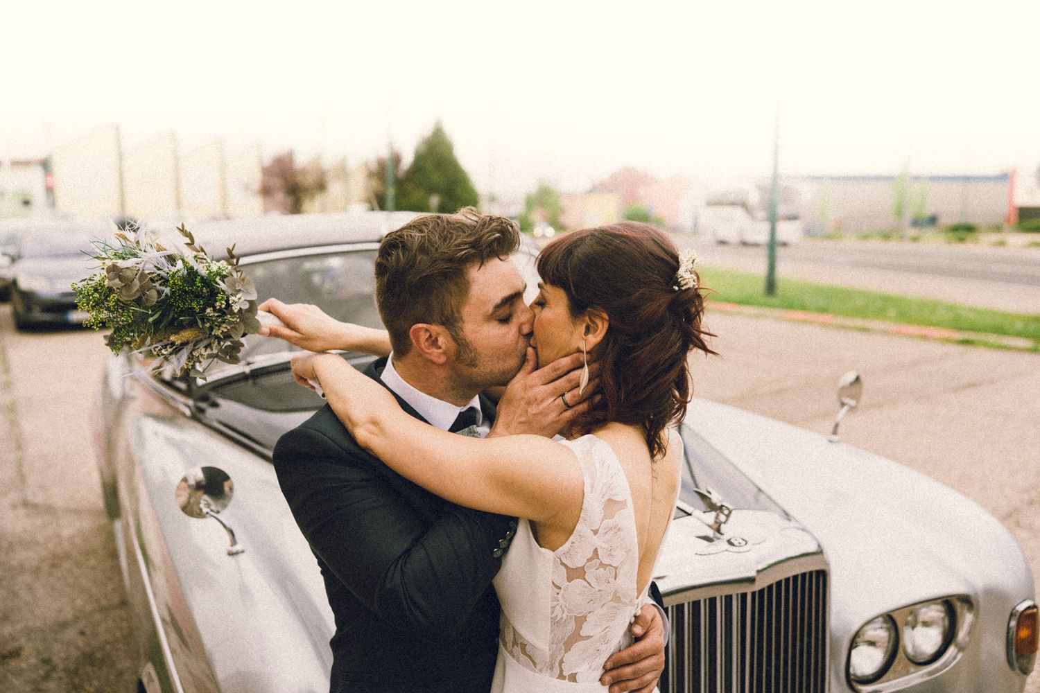 Bride and groom sharing a romantic kiss beside a classic white Rolls-Royce on their wedding day.