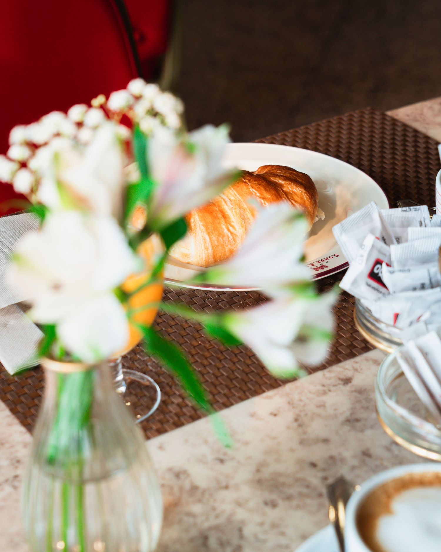 Elegant cafe table with a fresh flower vase, croissant on a plate, and a cappuccino.