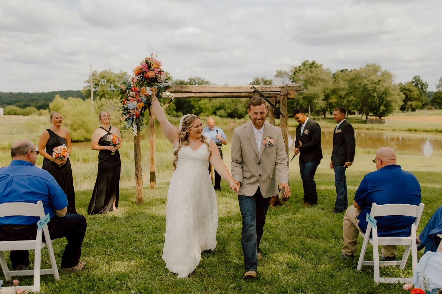 Joyful bride and groom walk down the aisle at an outdoor wedding ceremony surrounded by guests.