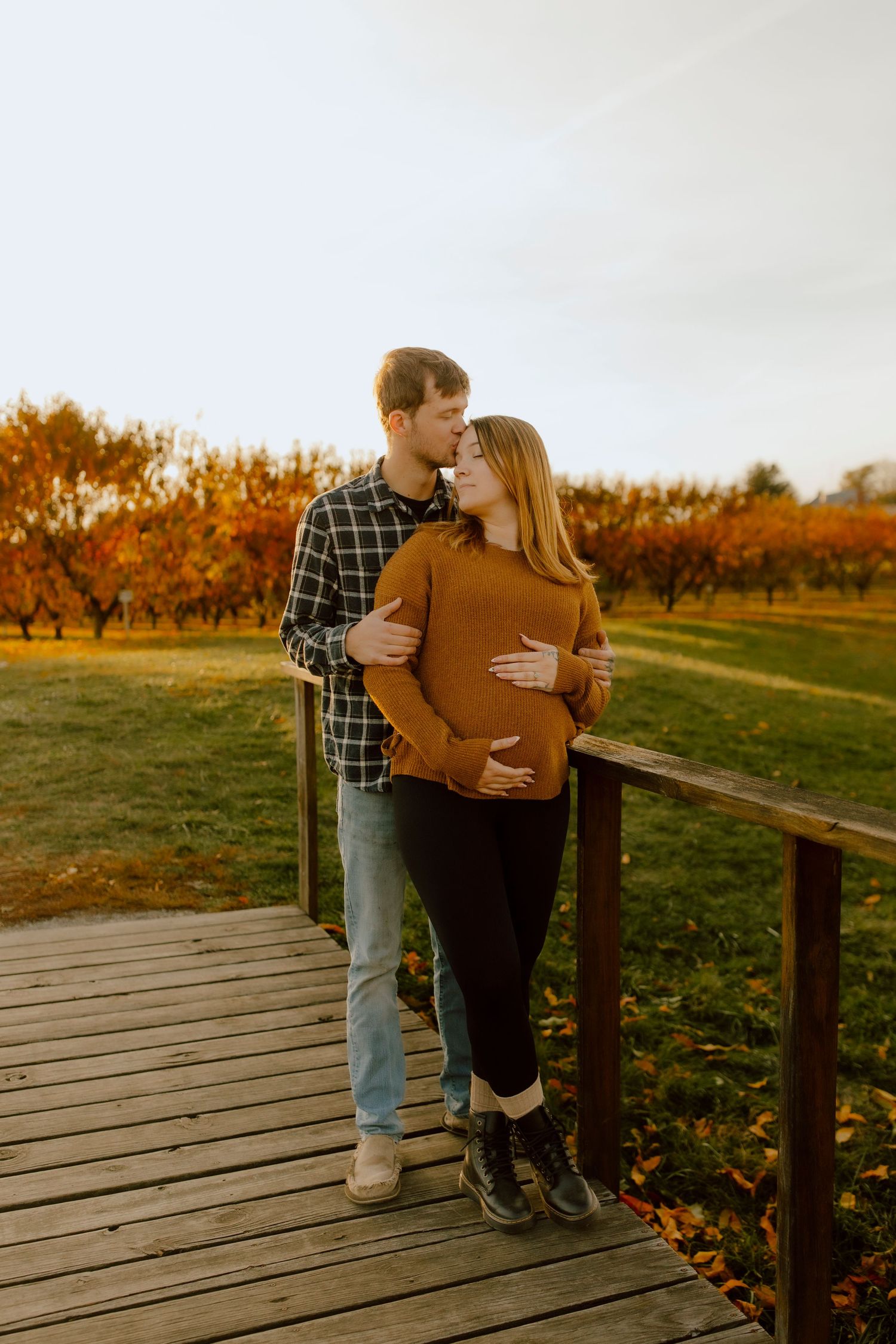 Couple sharing a tender kiss on a wooden bridge surrounded by colorful autumn foliage.