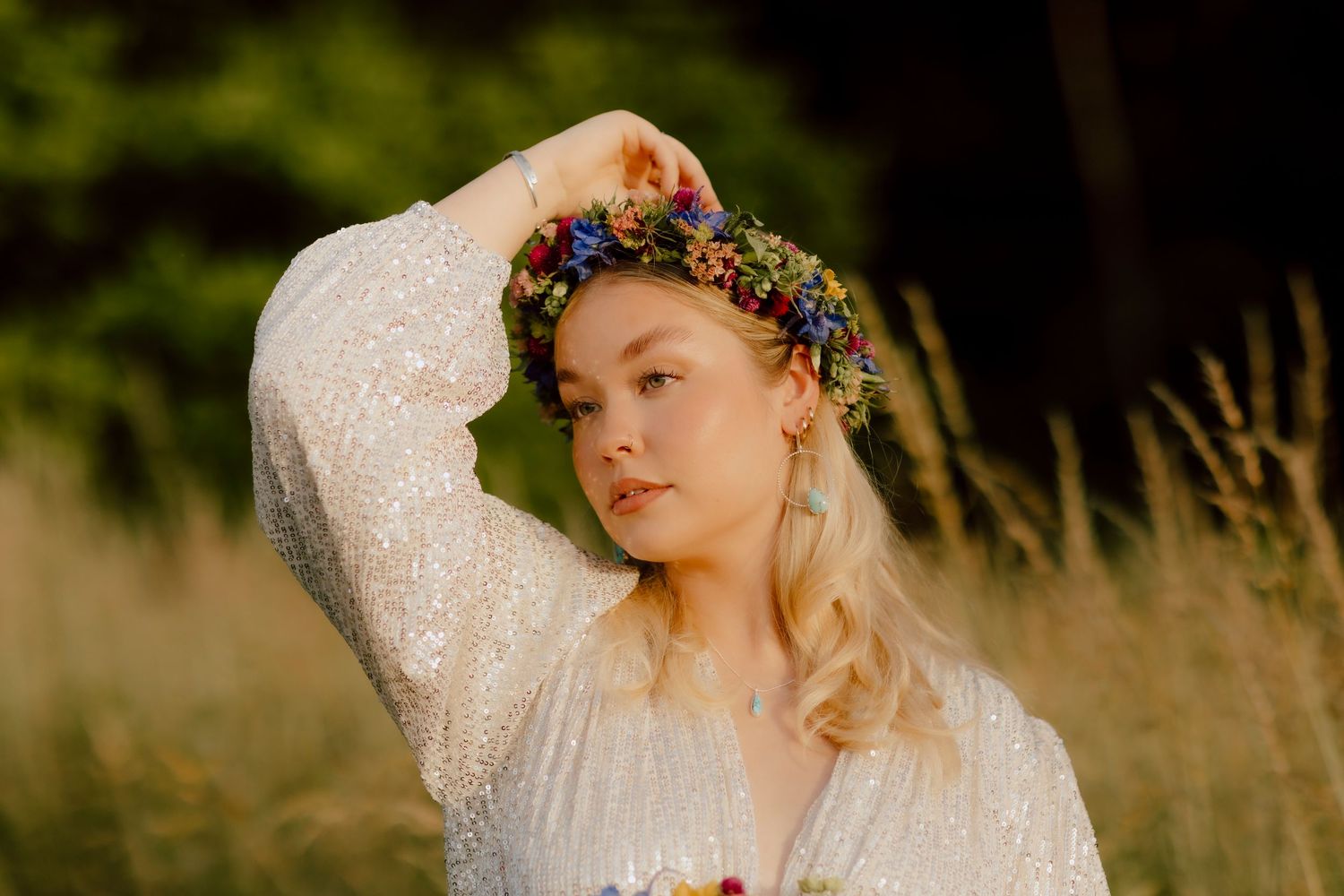 Young blonde woman wearing a floral crown and white lace dress poses in a golden field.