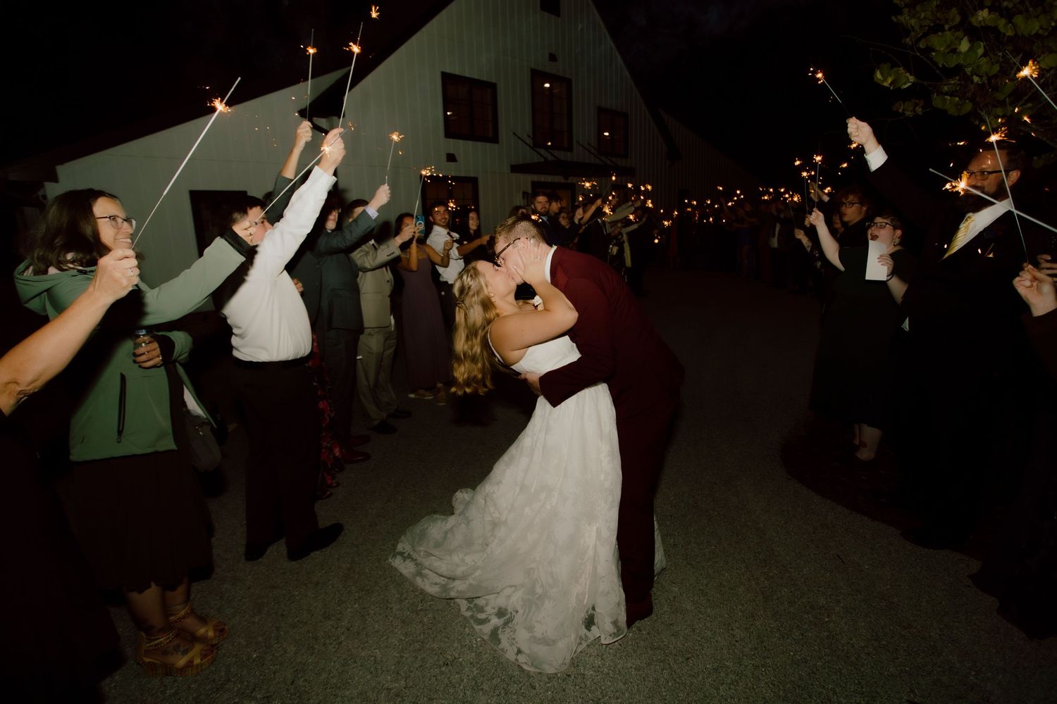 Bride and groom share romantic kiss during sparkler exit at outdoor evening wedding reception.