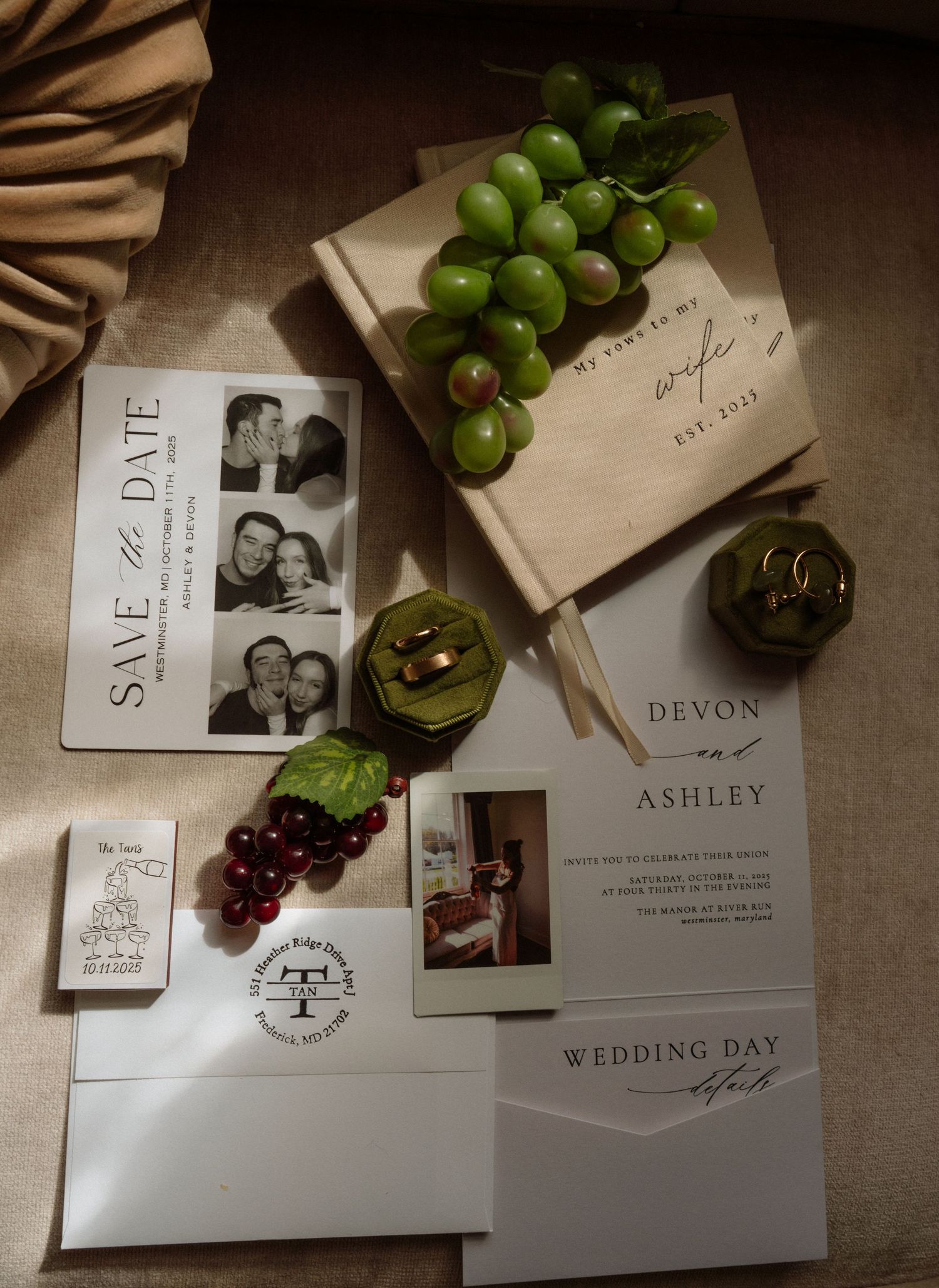 Elegant wedding stationery flat lay featuring save the date cards, invitations for Devon and Ashley, rings, and green grapes.