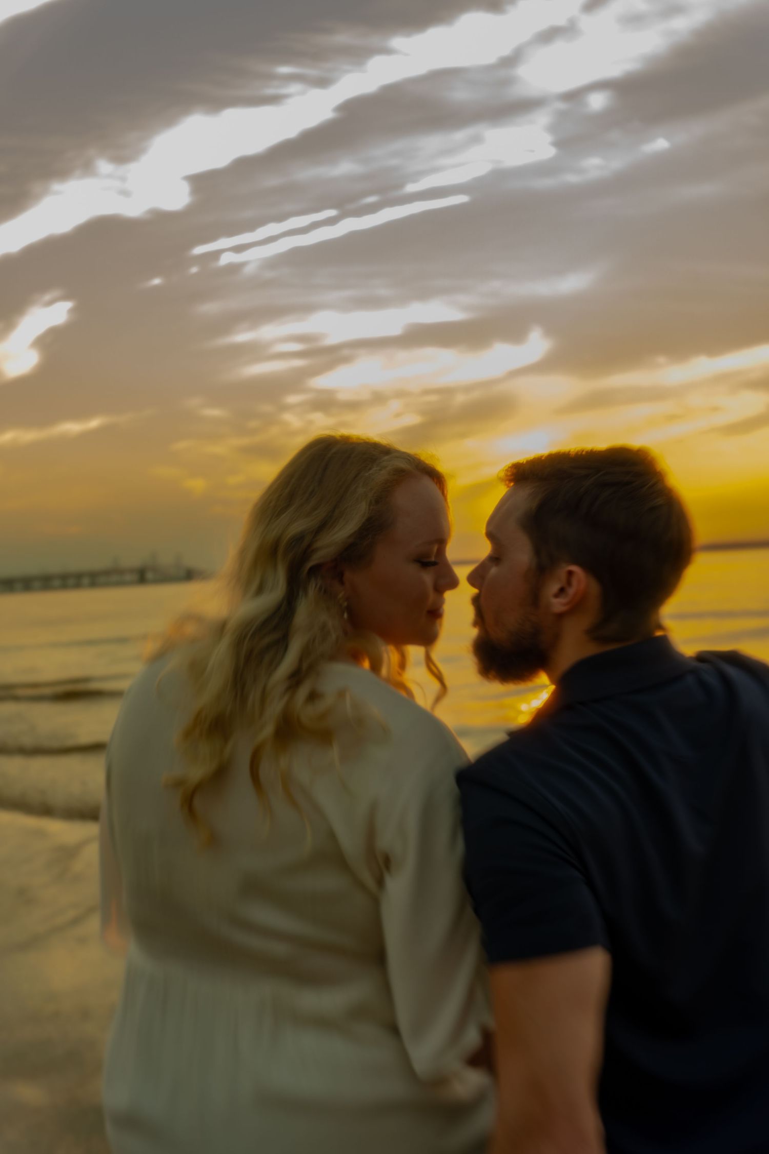 Couple sharing a romantic moment at sunset on the beach with golden sky and ocean waves in the background.